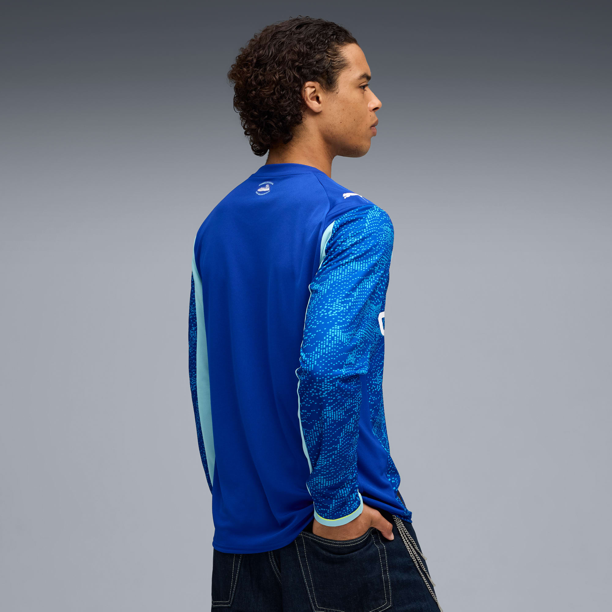 Un mannequin pose sur fond gris, portant un t-shirt bleu à manches longues et un jean foncé.