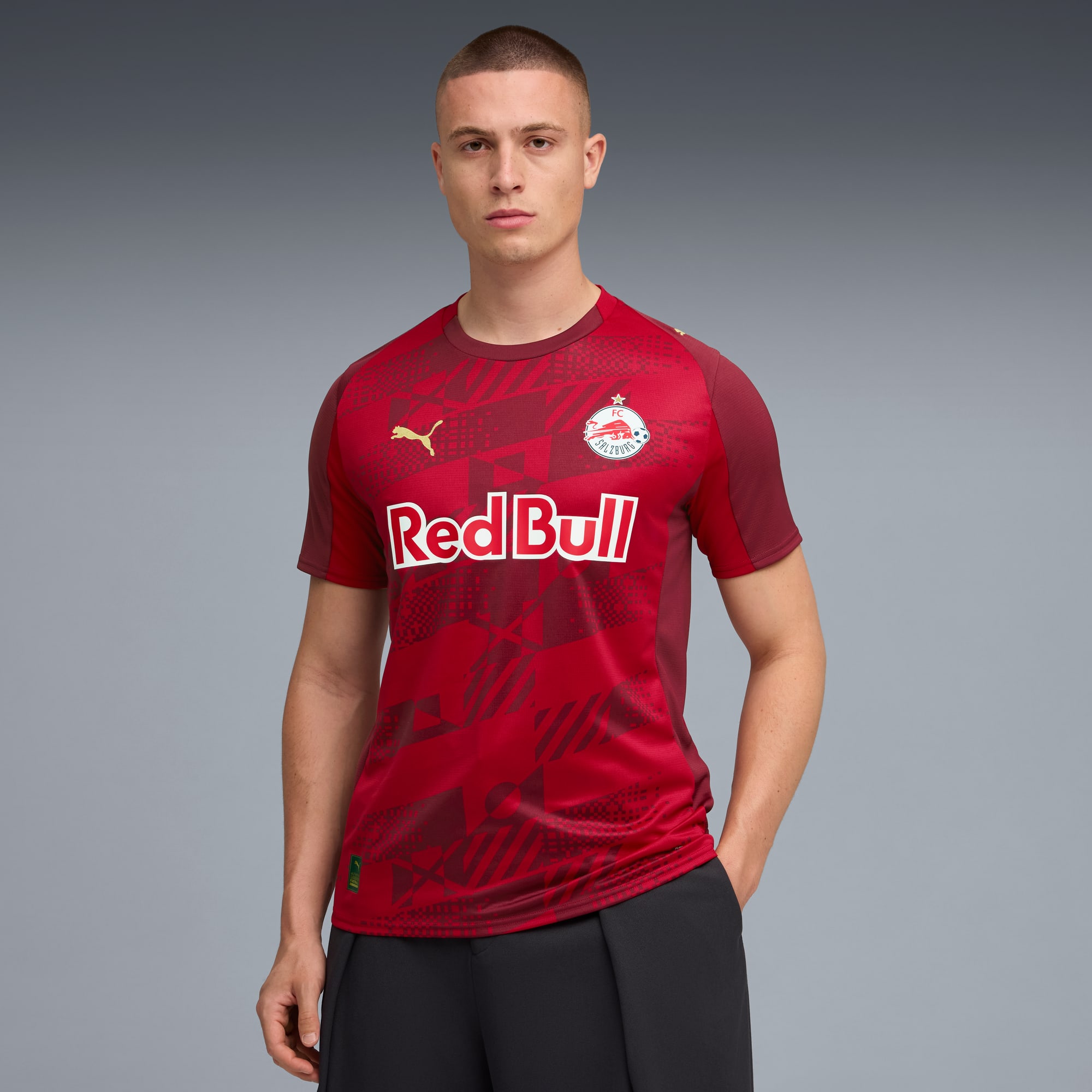 Su sfondo grigio, un modello indossa una t-shirt rossa Red Bull e pantaloni neri.