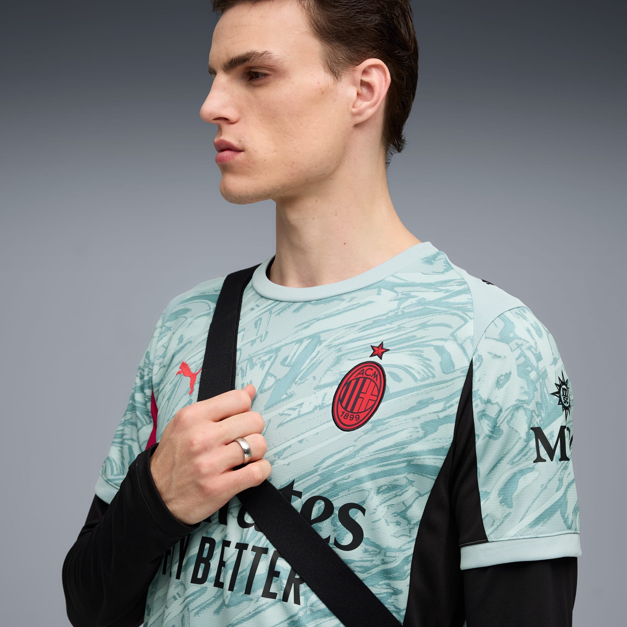 A model in front of a grey background wearing a patterned top and a black strap.