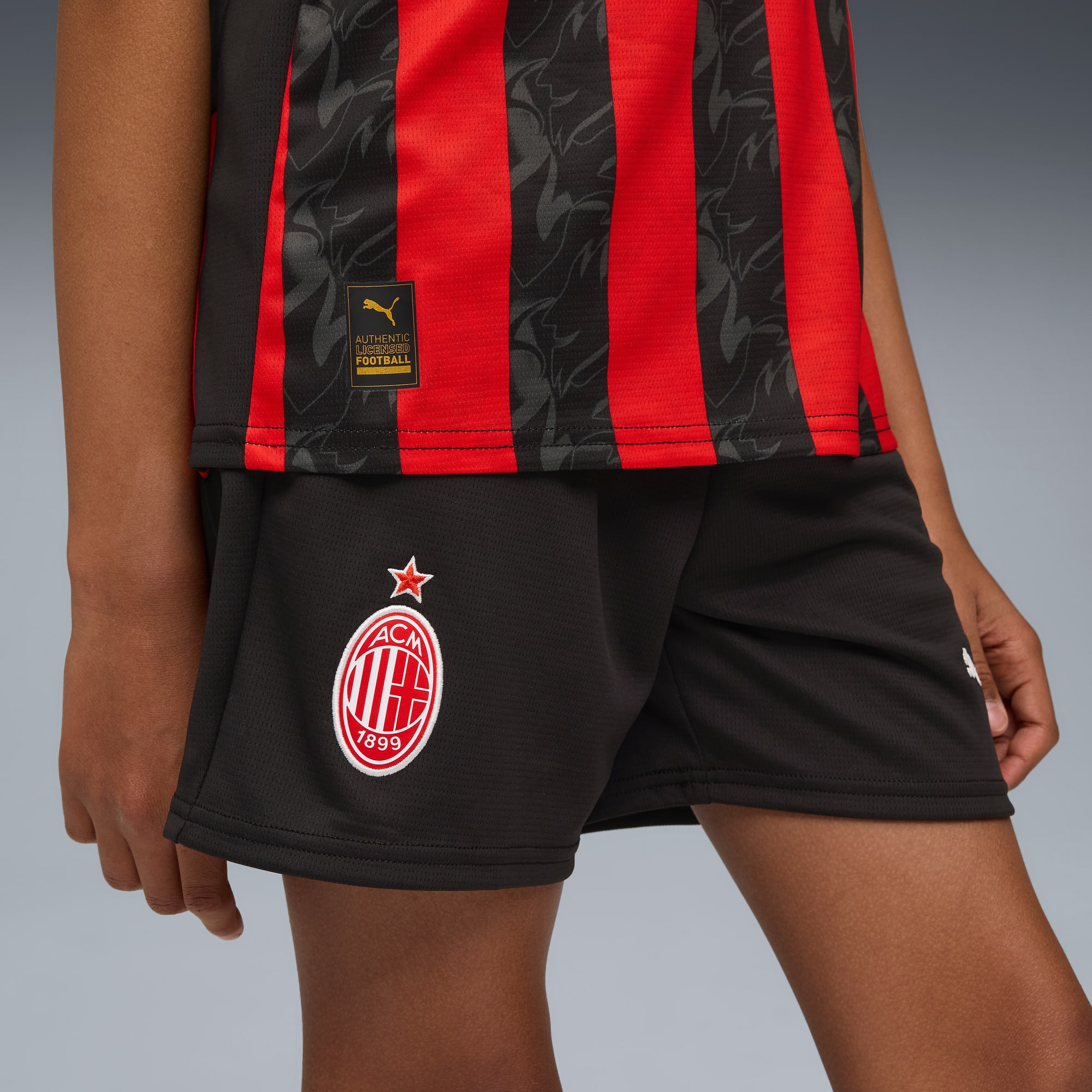 Vor einem grauen Hintergrund trägt ein Model ein rot-schwarzes Oberteil mit schwarzen Shorts.