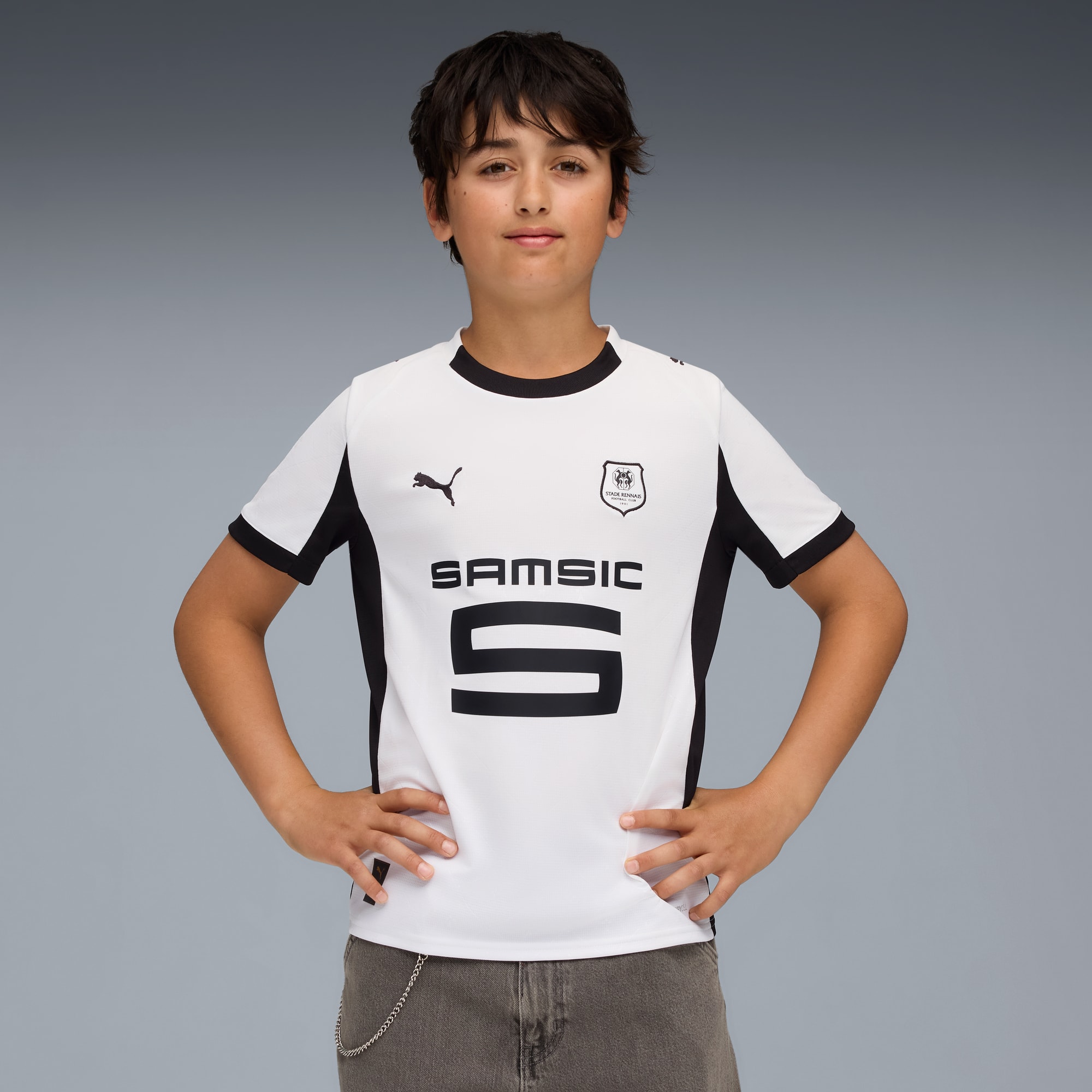 Vor grauem Hintergrund posiert ein Kind in einem weiss-schwarzen Fussballtrikot.