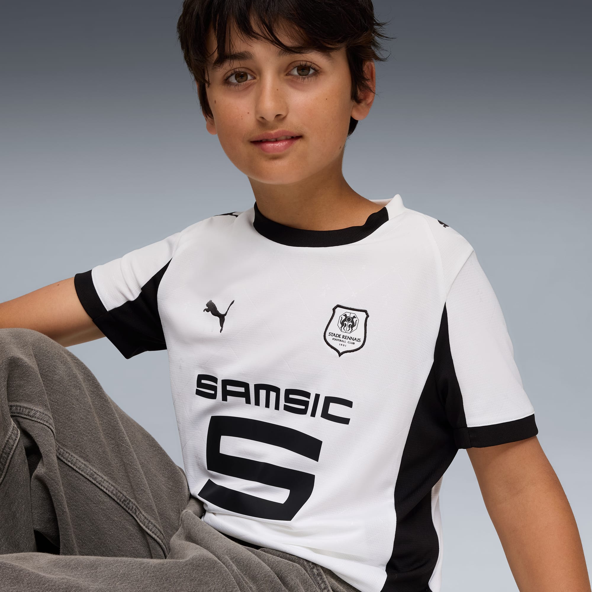 Ein Model posiert vor grauem Hintergrund in einem weiss-schwarzen Fussballtrikot.