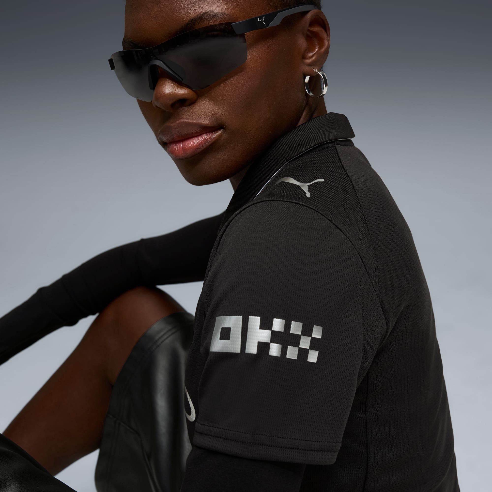Un modèle avec des lunettes de soleil pose sur fond gris, portant une chemise noire.
