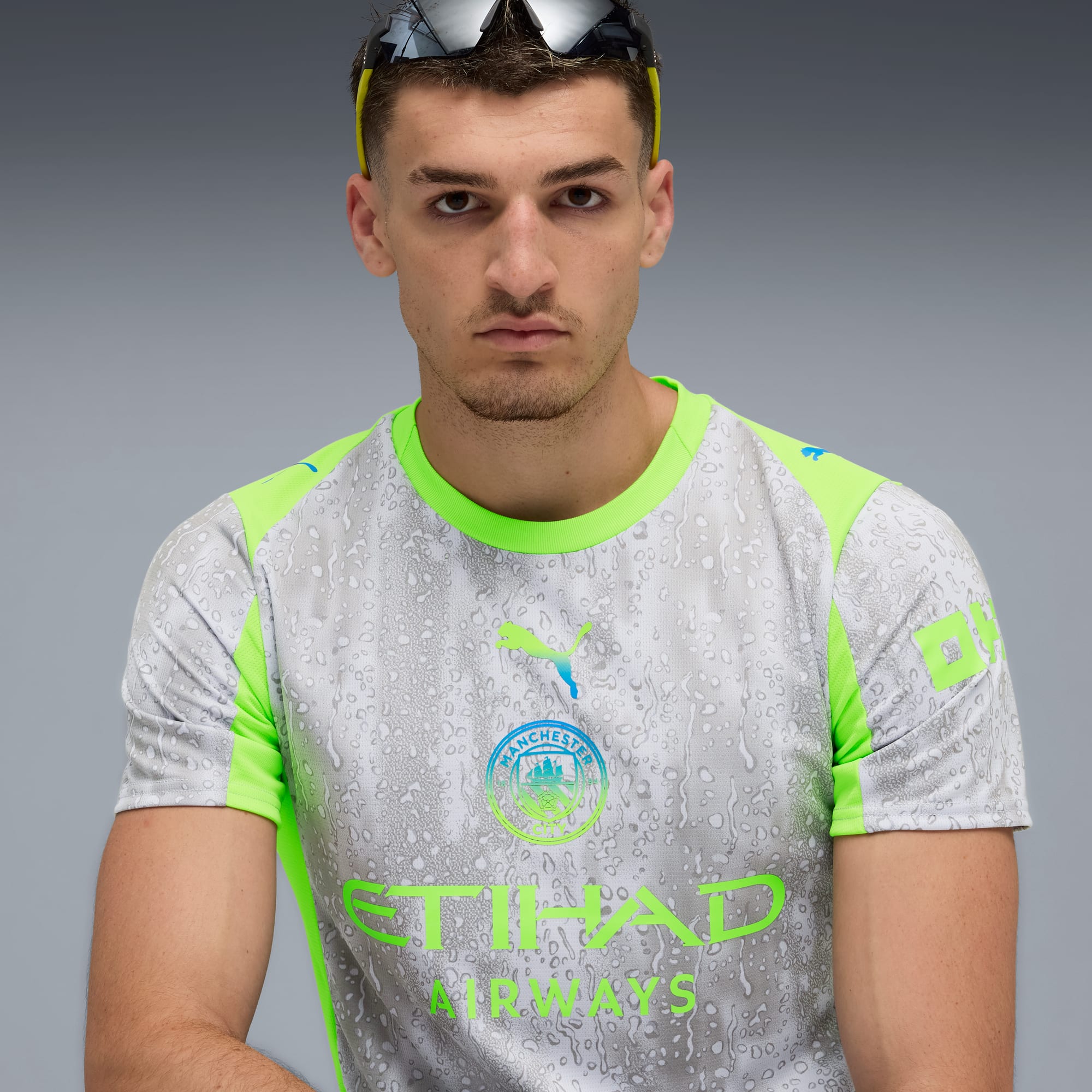 Vor grauem Hintergrund trägt ein Model eine Sonnenbrille und ein gemustertes Shirt.