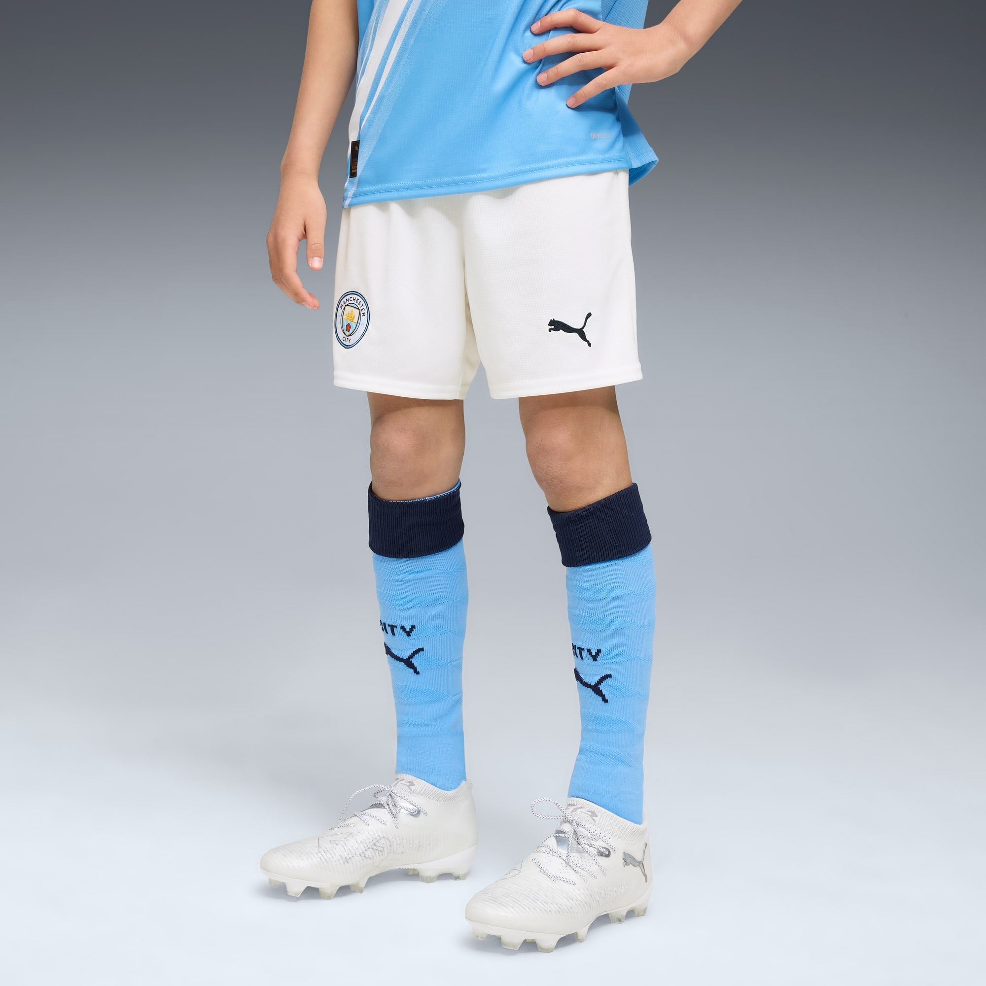 Su uno sfondo grigio, un modello indossa un kit da calcio con calzini azzurri e scarpe bianche.