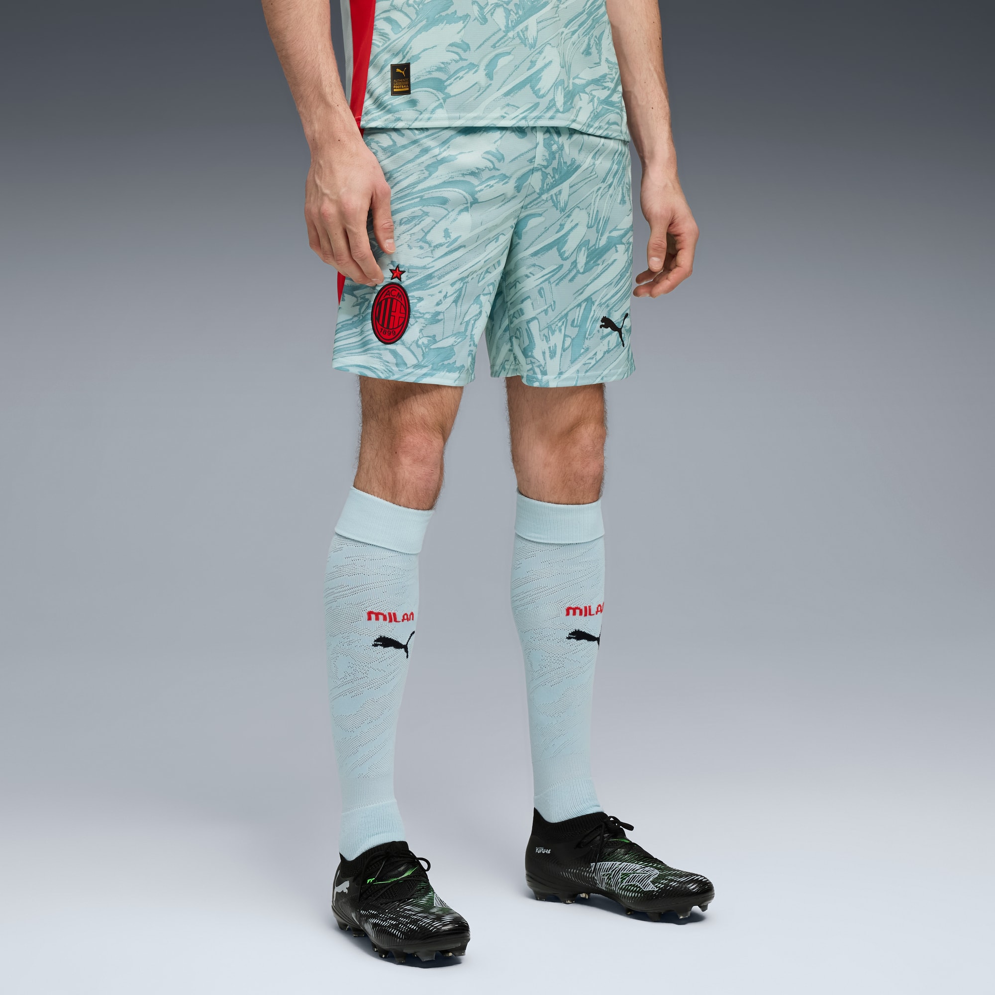 Sur fond gris, un modèle porte un t-shirt à motifs, un short, des chaussettes et chaussures.