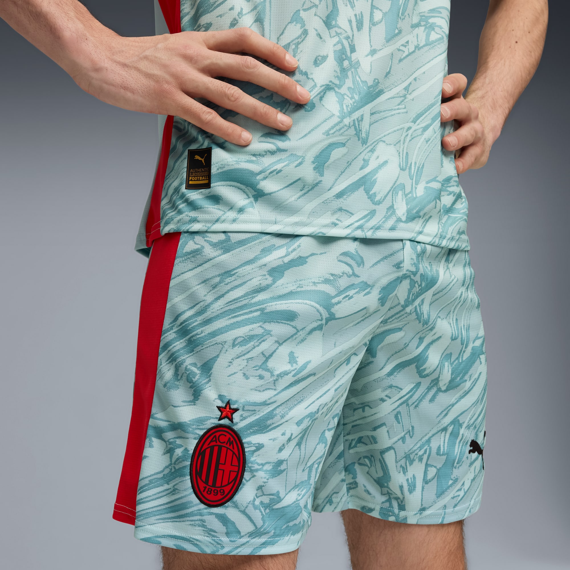 Sur fond gris, un modèle pose en t-shirt à motifs et short avec des accents rouges.