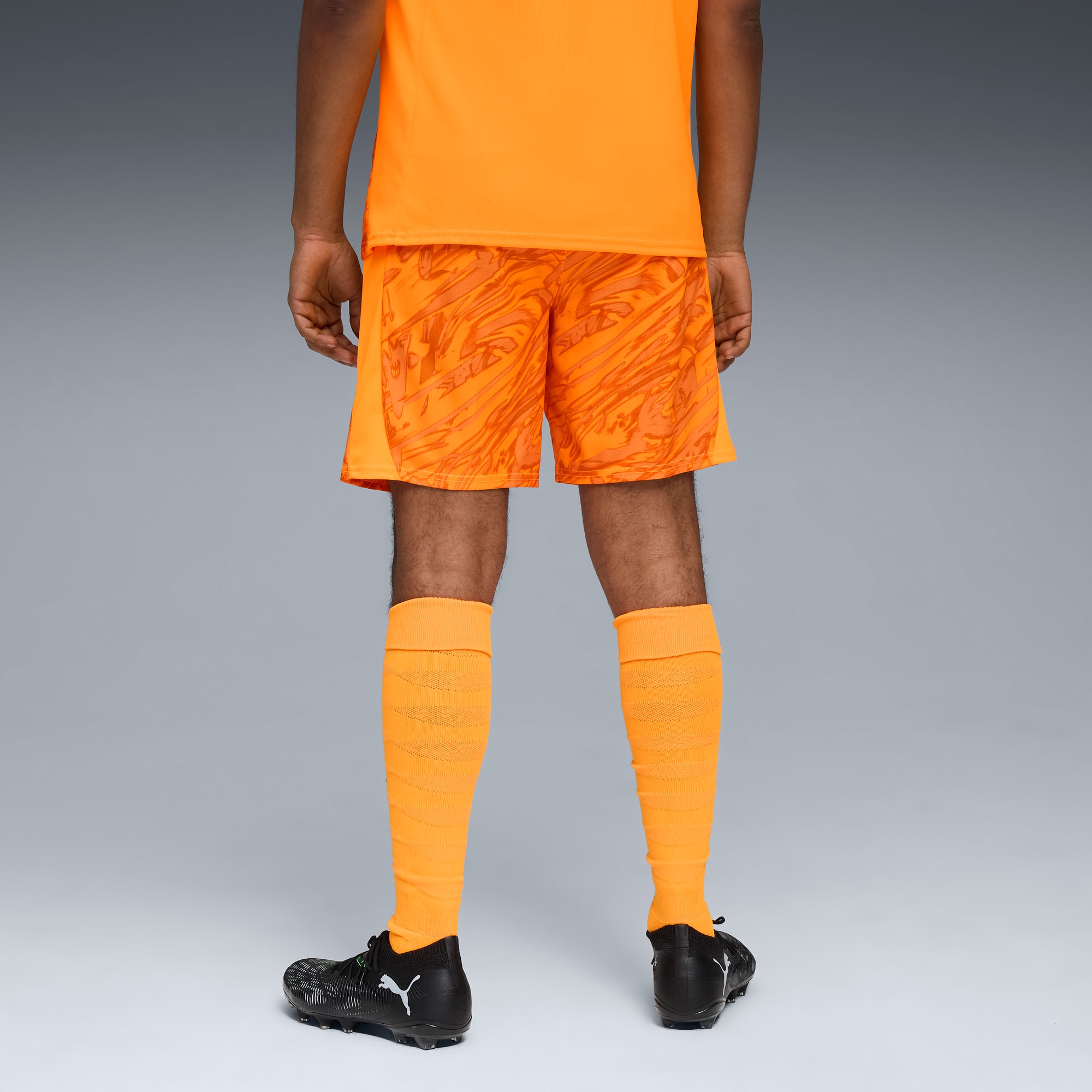 Un modèle sur fond gris porte un équipement orange avec chaussettes et chaussures noires.