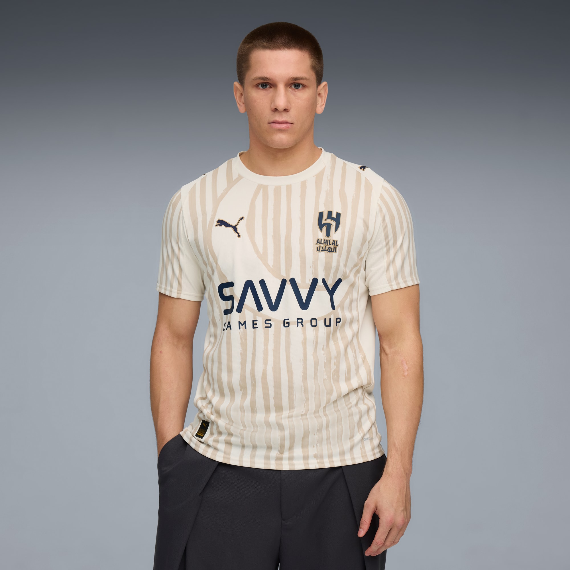 Un modello su sfondo grigio indossa una t-shirt a righe con loghi e pantaloni scuri.