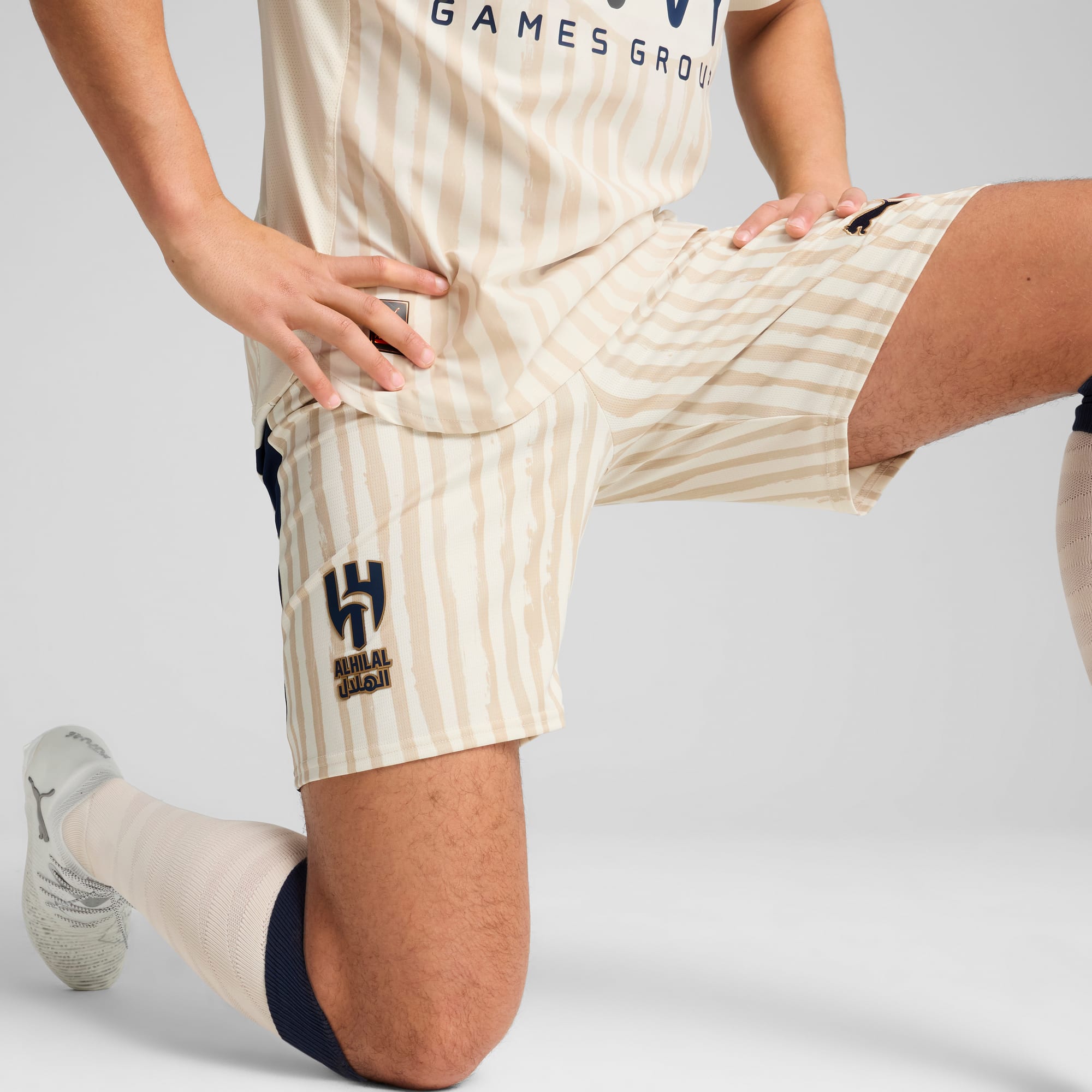 Vor einem weißen Hintergrund kniet ein Model mit gestreiften Shorts, Socken und Turnschuhen.