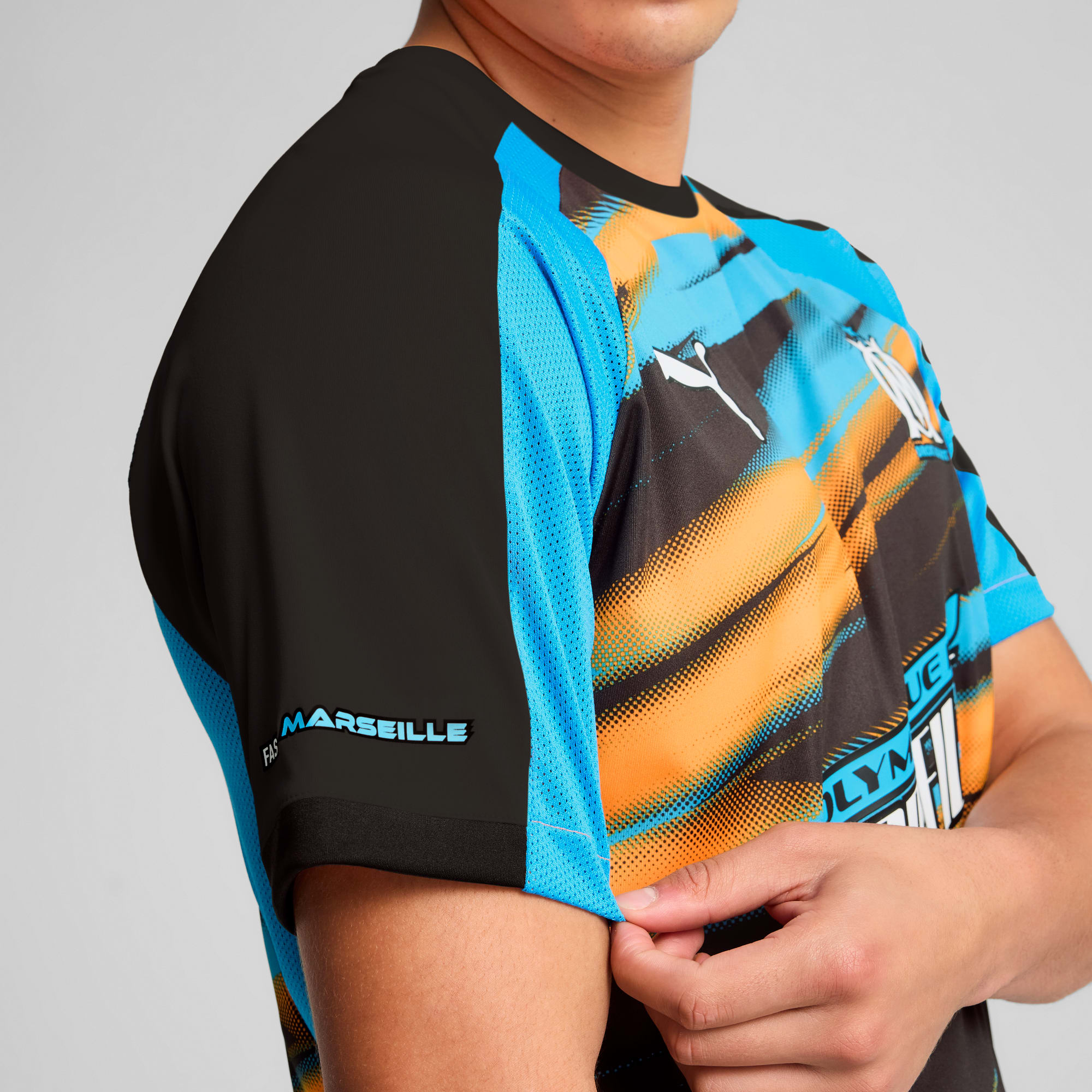 Tegen een grijze achtergrond past iemand een zwart, blauw en oranje shirt met korte mouwen aan.