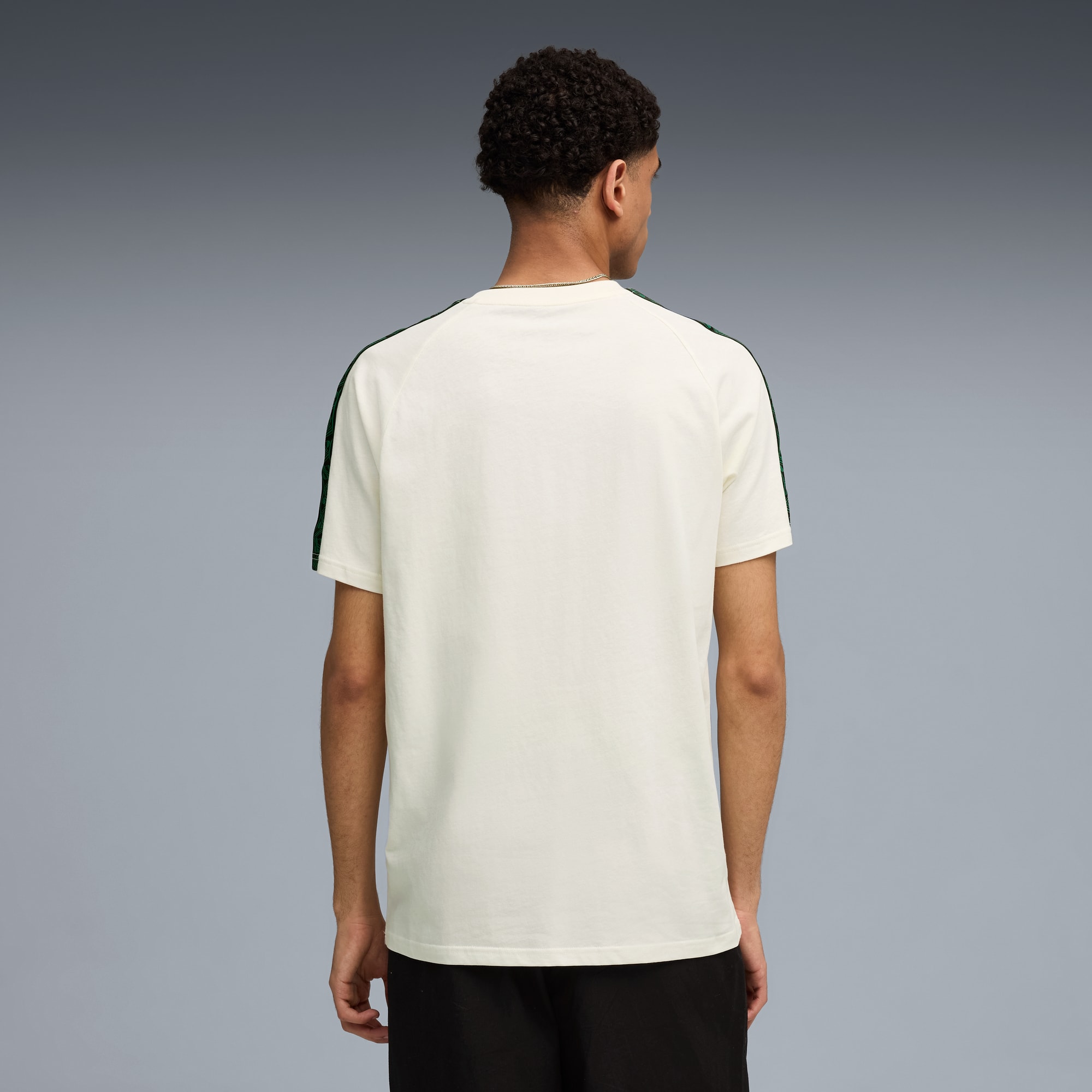 Un modelo de espaldas sobre gris, con camiseta blanca de rayas verdes y pantalón corto negro.