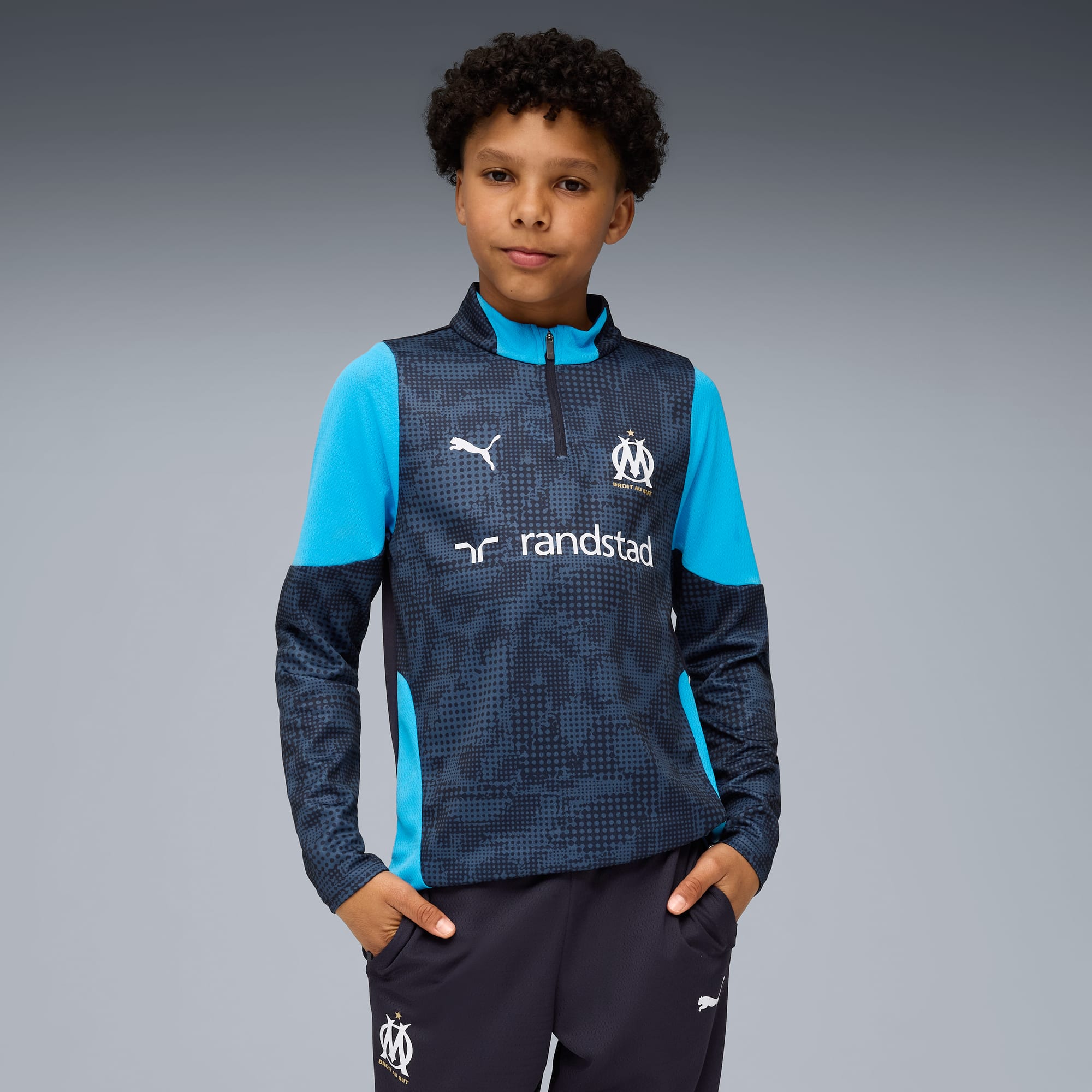 Een jong model poseert tegen een grijze achtergrond in een trainingspak met patroon.