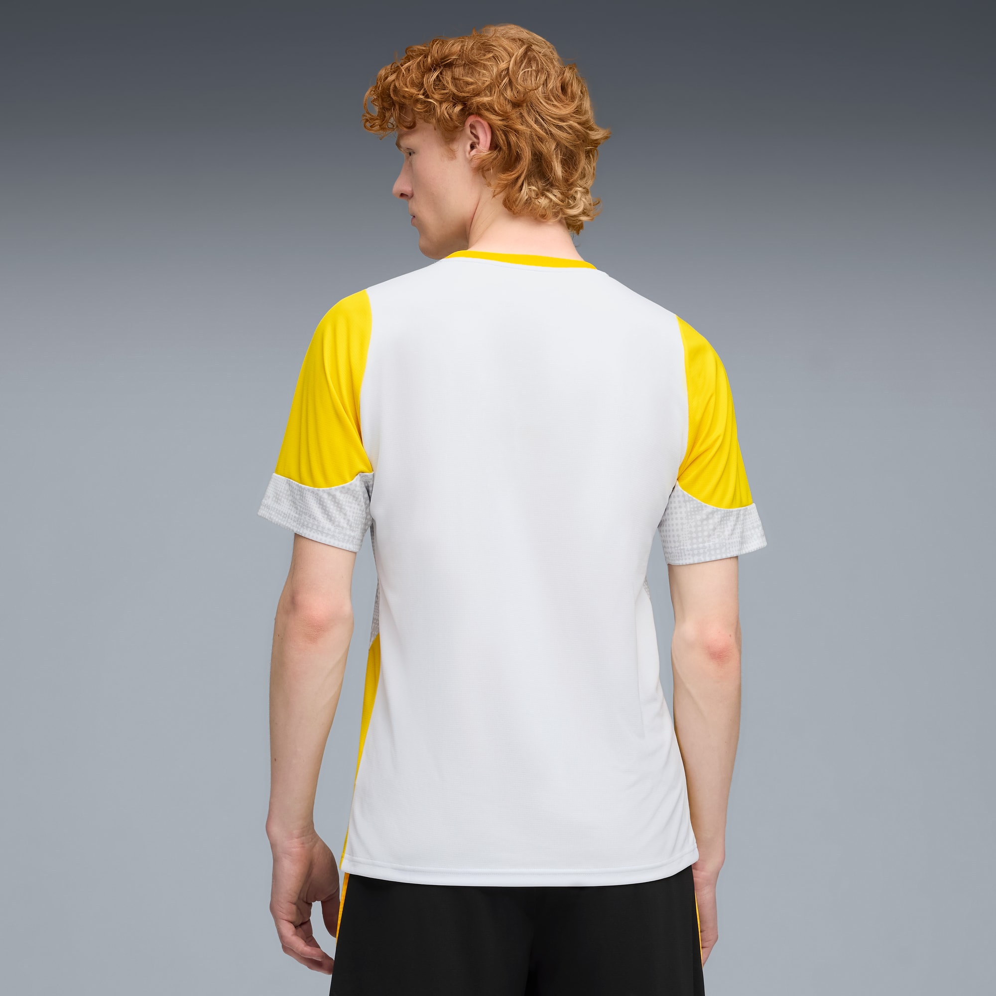 Vor grauem Hintergrund trägt ein Model ein weiss-gelb-graues Shirt und schwarze Shorts.
