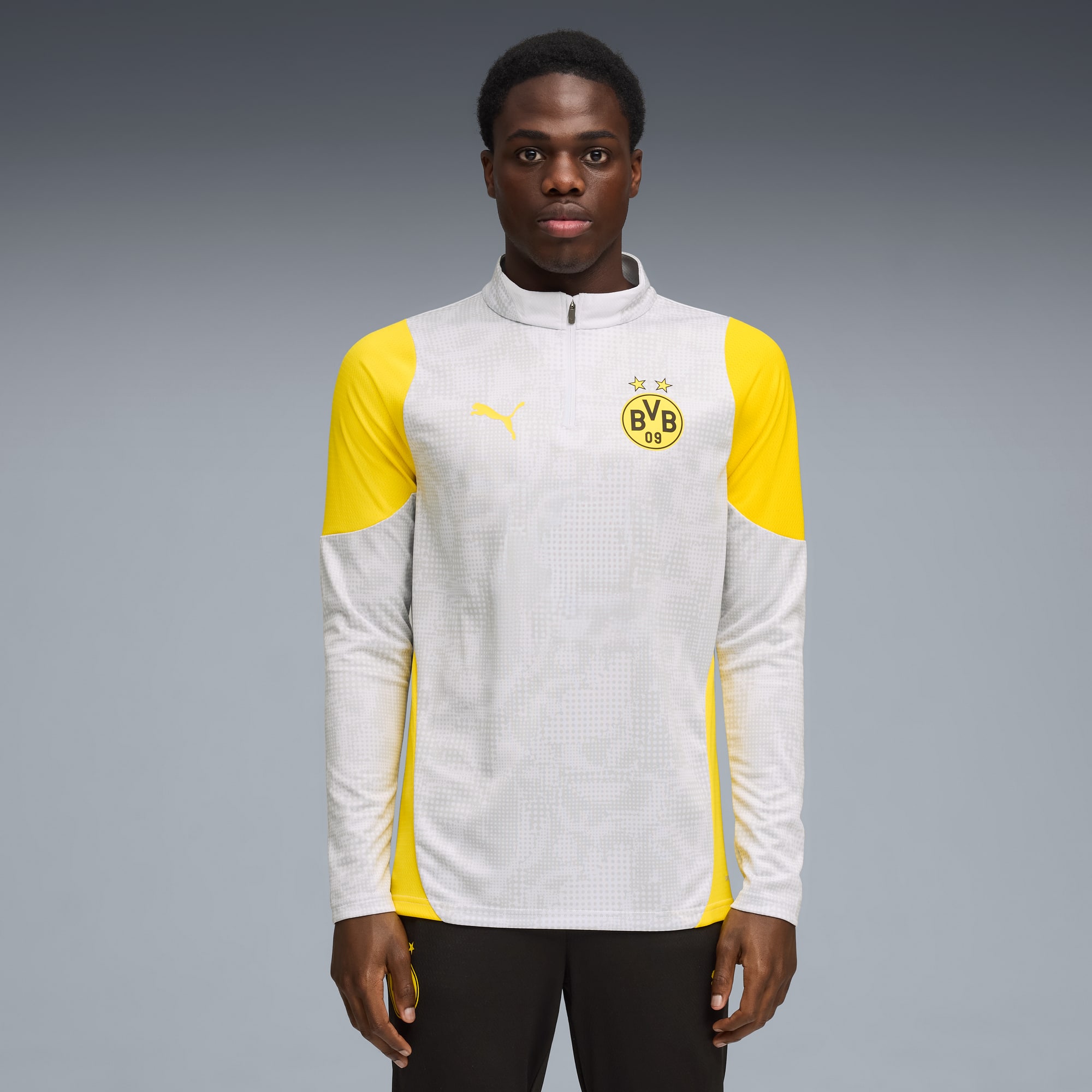 Un mannequin pose sur fond gris, portant un haut à manches longues blanc et jaune.