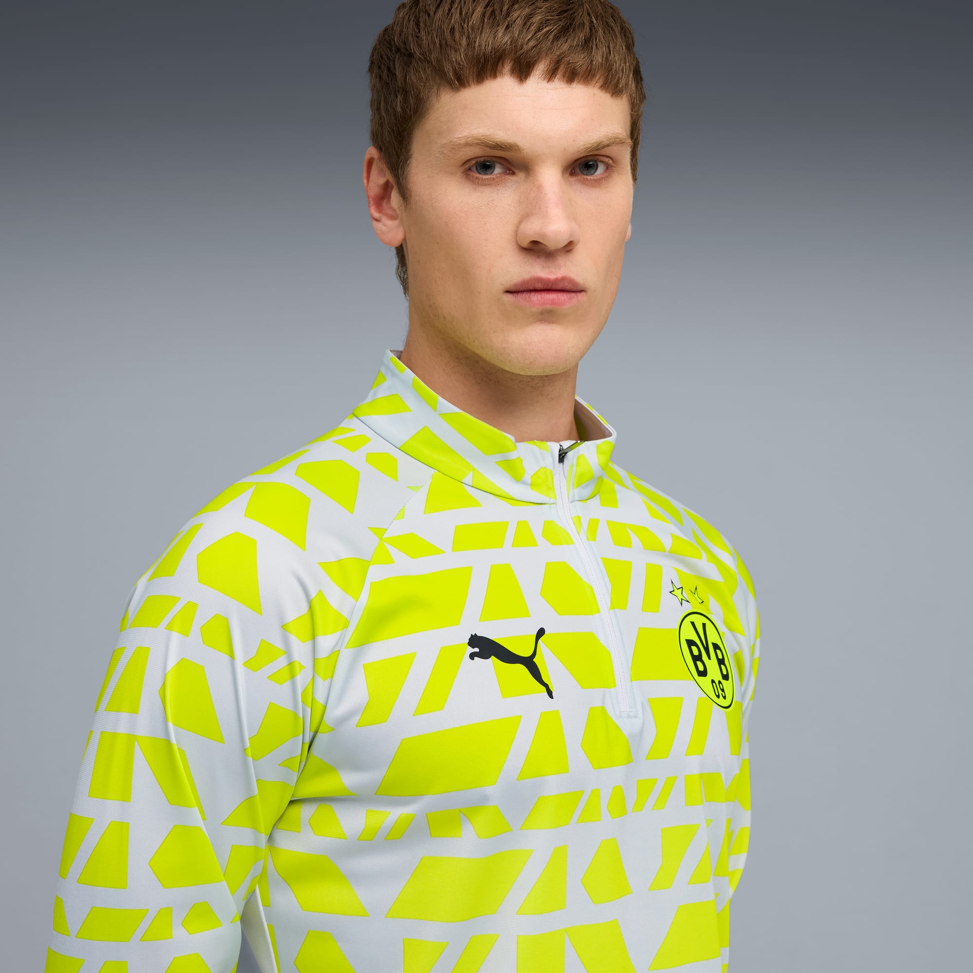 Op een grijze achtergrond draagt een model een wit-geel shirt met lange mouwen en patroon.