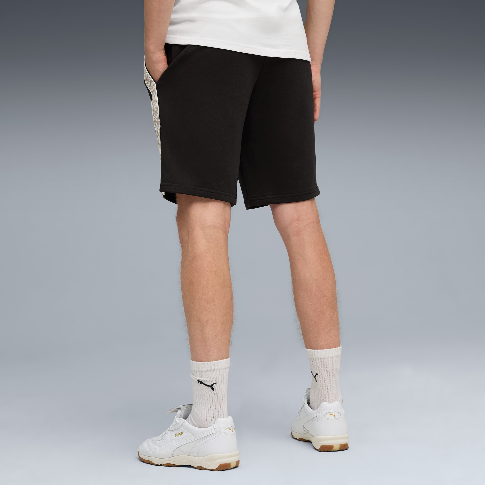 Un modèle sur fond gris porte tee-shirt blanc, short foncé, chaussettes et baskets blanches.