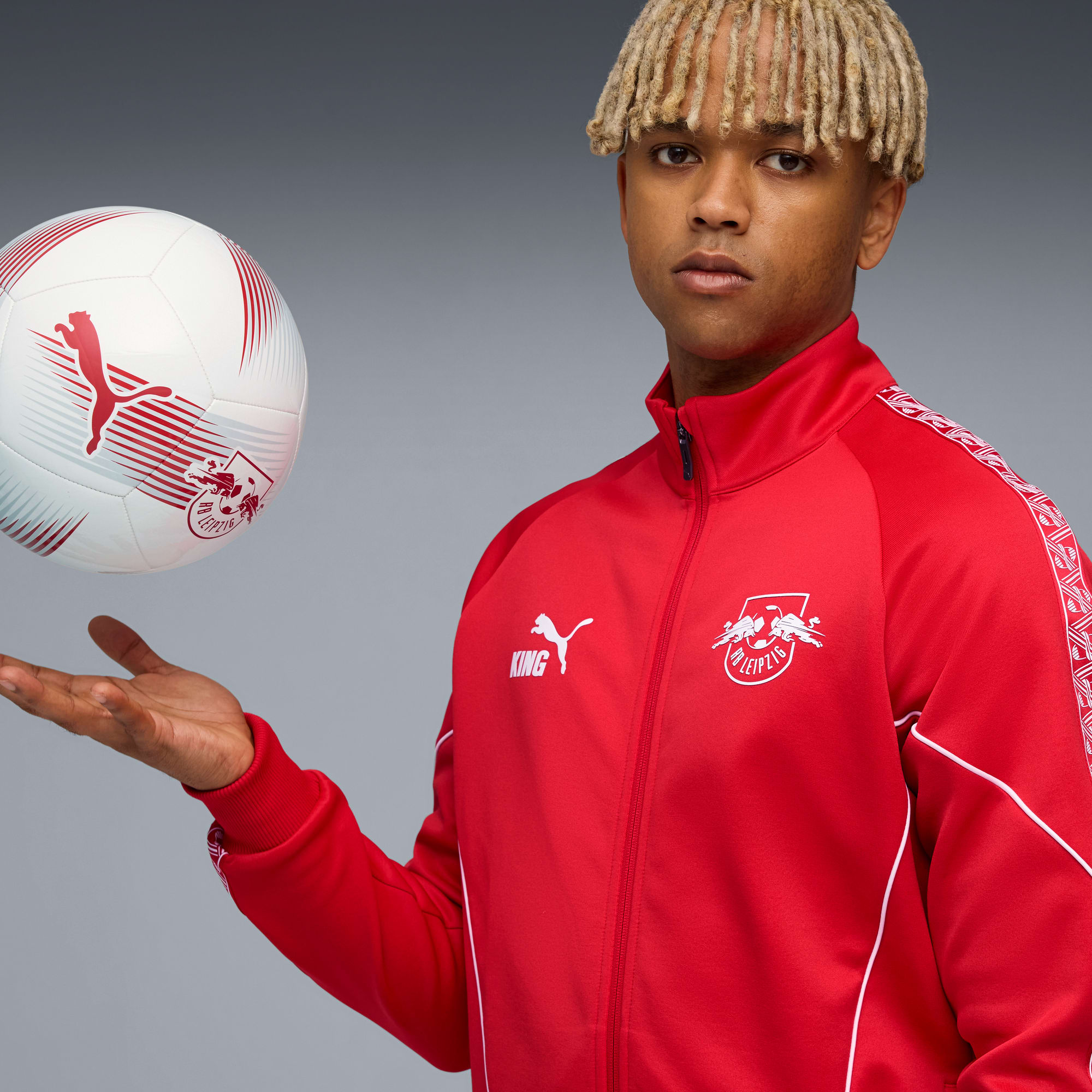 Op grijs, model met dreadlocks balanceert voetbal in rood Leipzig-jack.