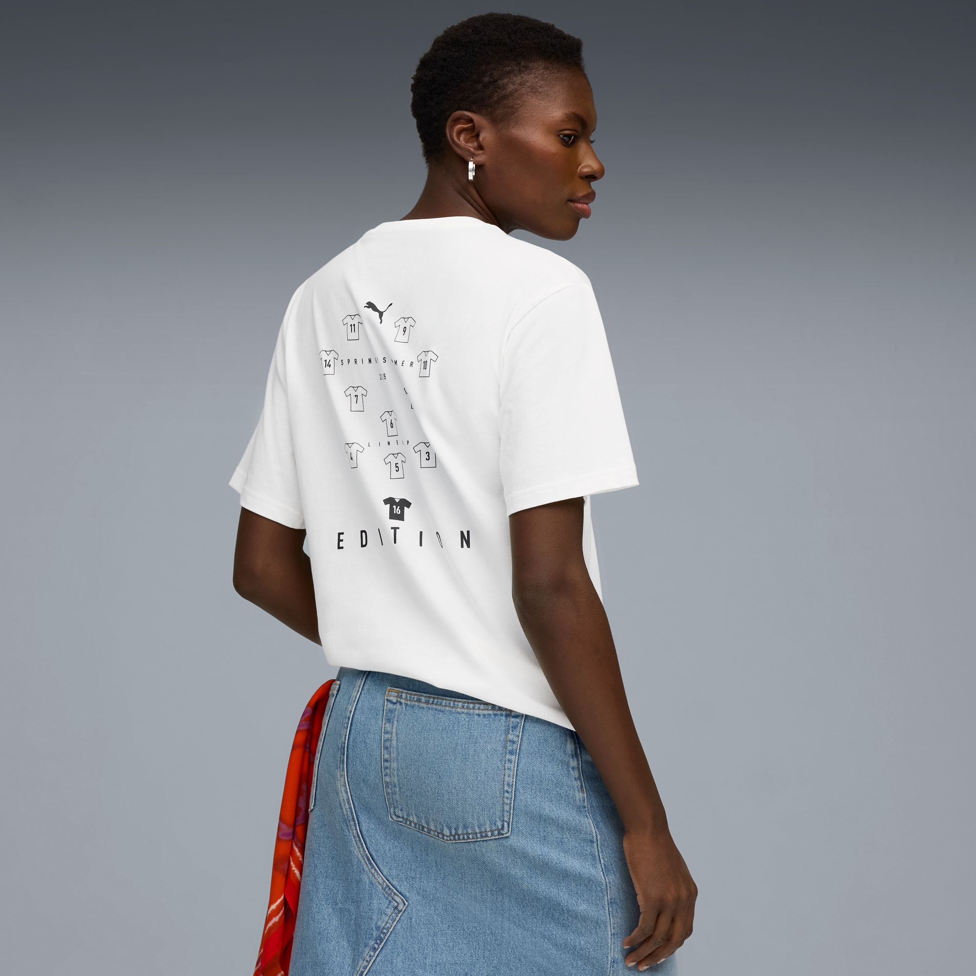 Tegen een grijze achtergrond draagt een model een wit T-shirt met print en een denim rok.