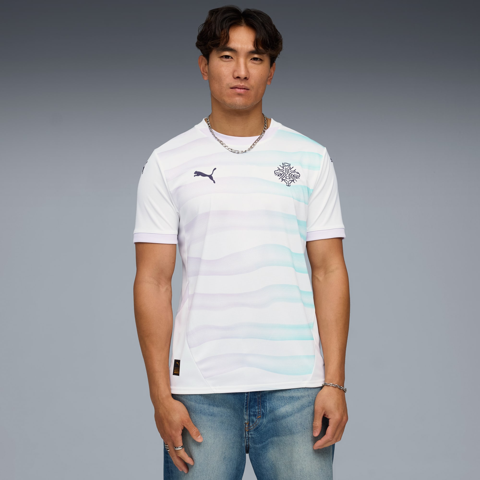Vor grauem Hintergrund posiert ein Model mit gemustertem, weißen T-Shirt und Jeans.