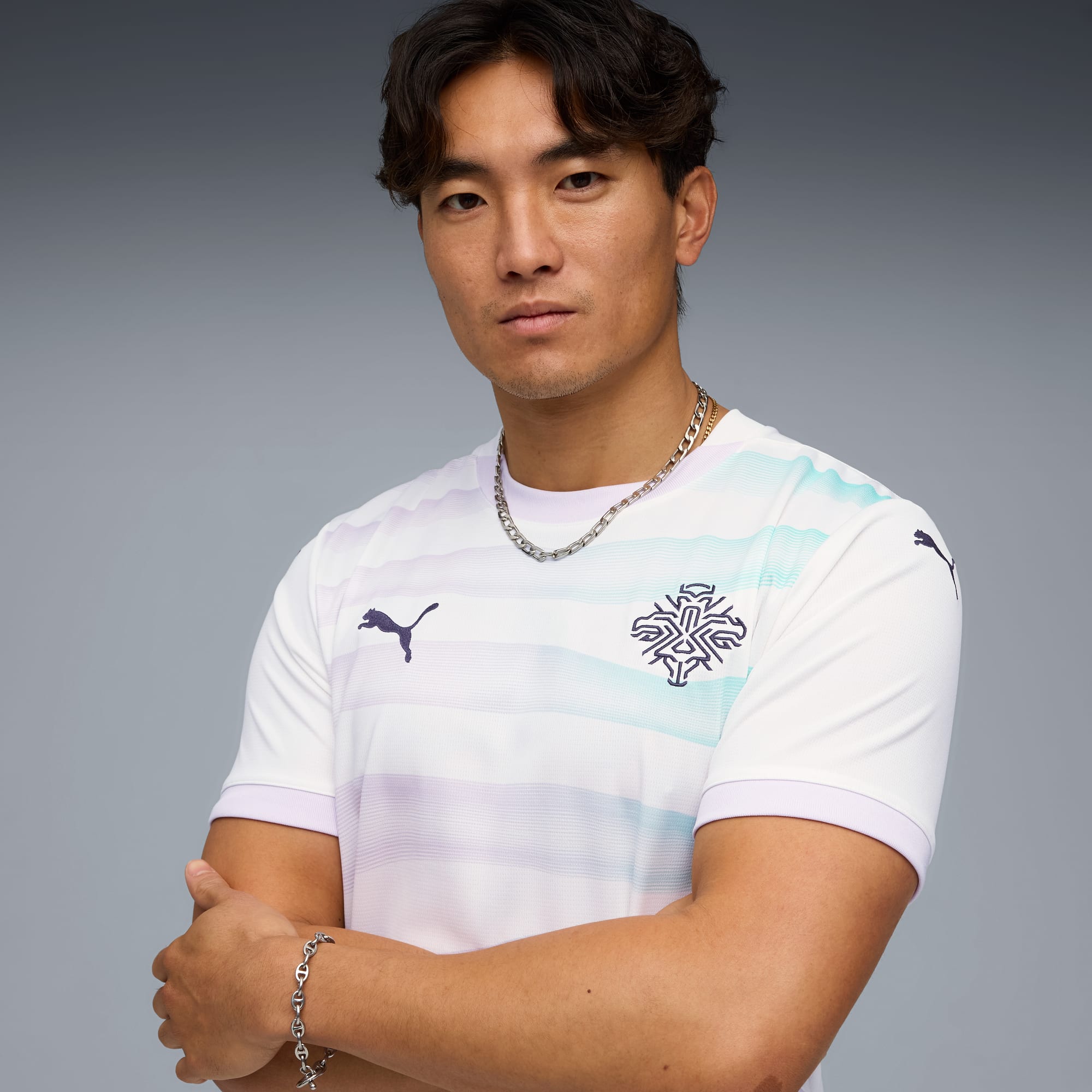 Un modelo posa con los brazos cruzados sobre un fondo gris, vistiendo una camiseta blanca estampada.