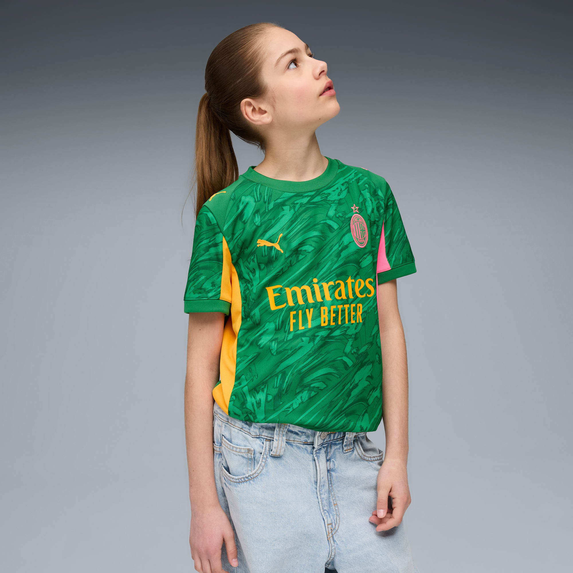 A model on grey looks up while wearing a green patterned t-shirt and denim jeans.