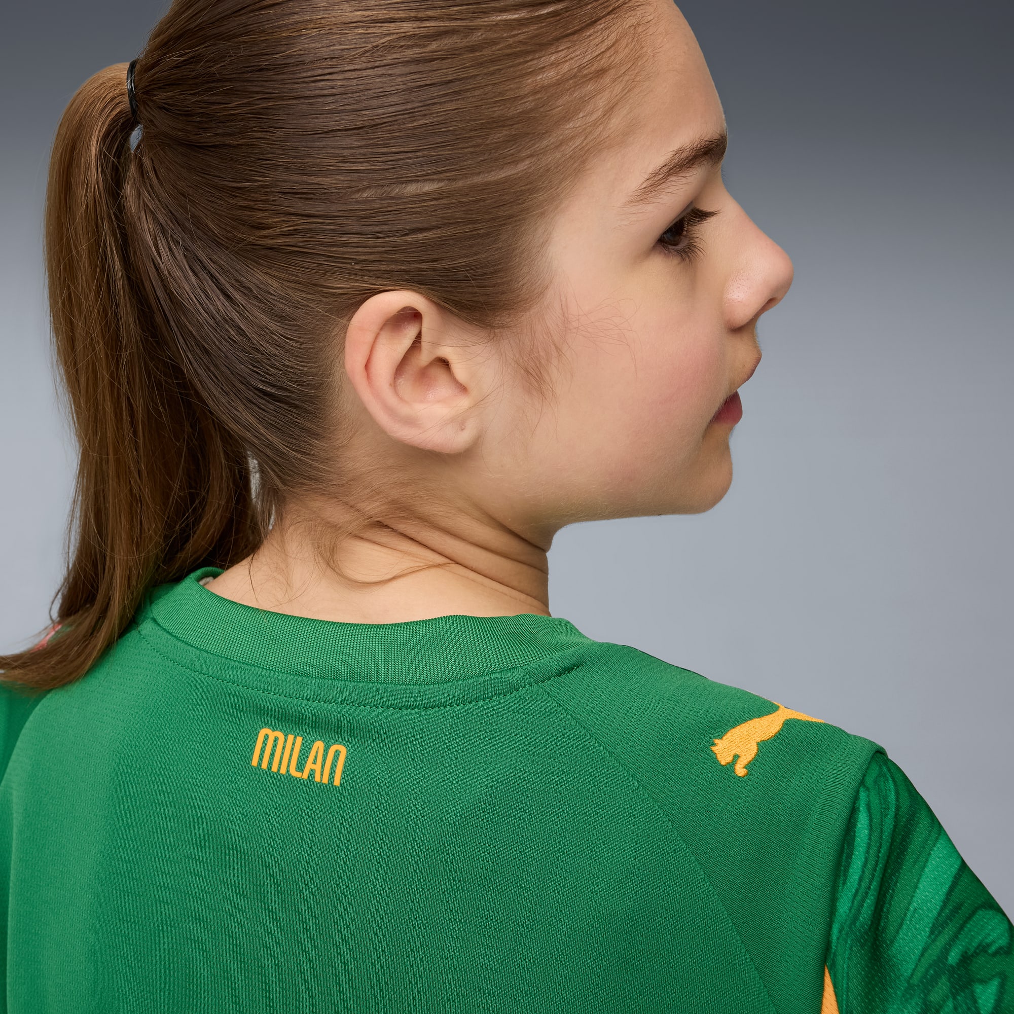 A child with ponytail, facing right, wears a green shirt with 'MILAN' text.