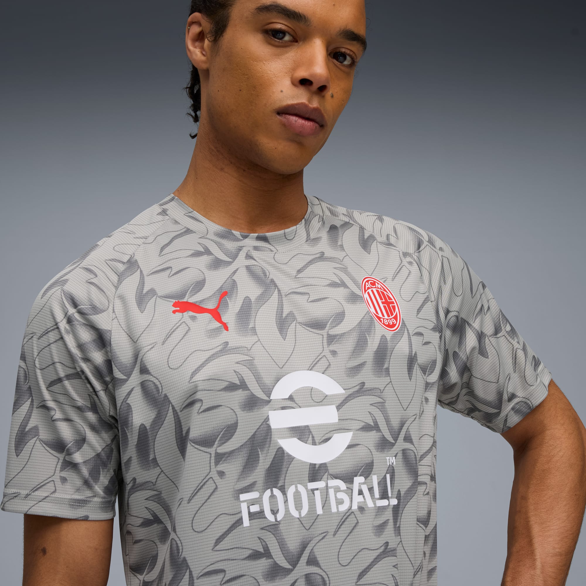 Un modello su sfondo grigio indossa una t-shirt grigia fantasia con logo ed emblema rossi.
