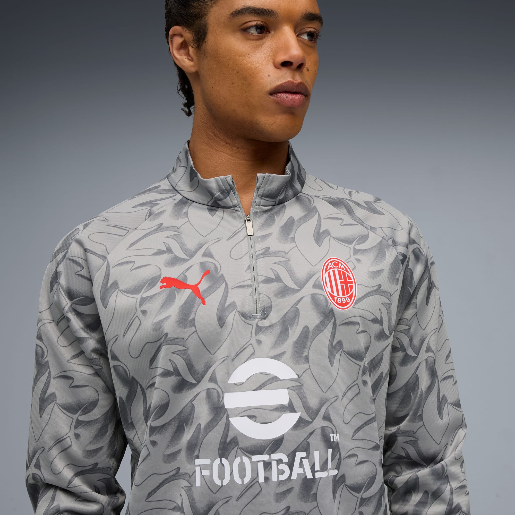 Sur fond gris, un mannequin porte un haut gris à motifs avec des logos rouges et blancs.
