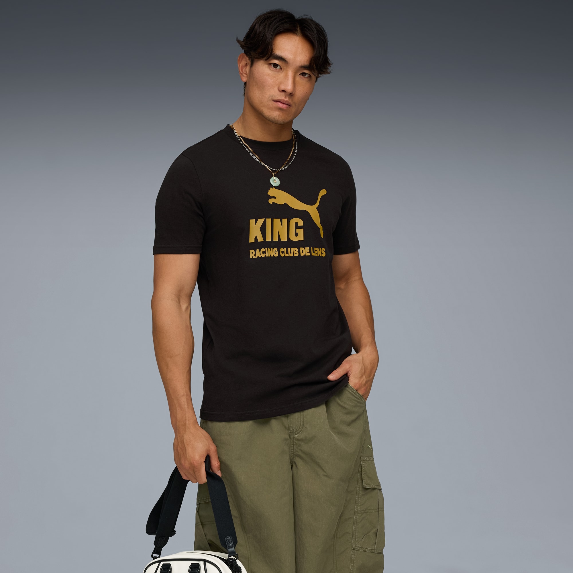 Sur fond gris, un mannequin pose avec un t-shirt graphique, un short et un sac.
