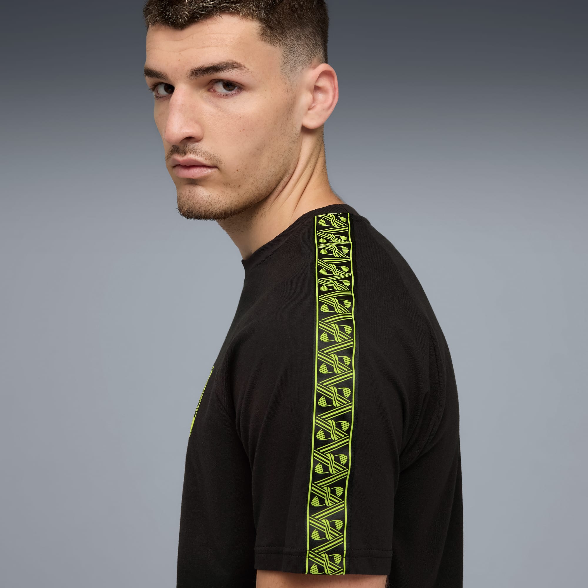 Un mannequin pose sur fond gris, portant un t-shirt noir à rayures vert néon.