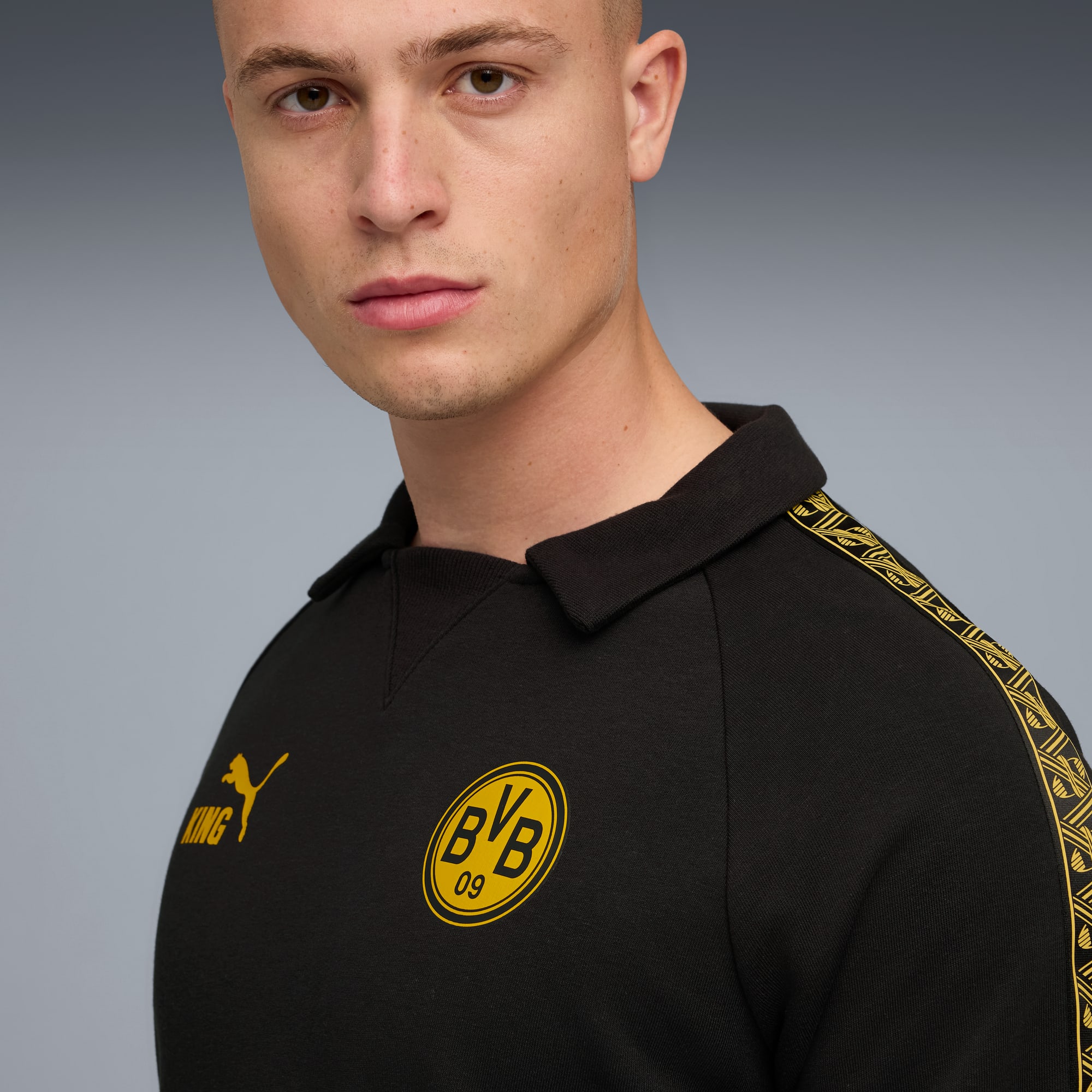 Ein Model vor grauem Hintergrund trägt ein schwarzes BVB Poloshirt mit gelben Akzenten.
