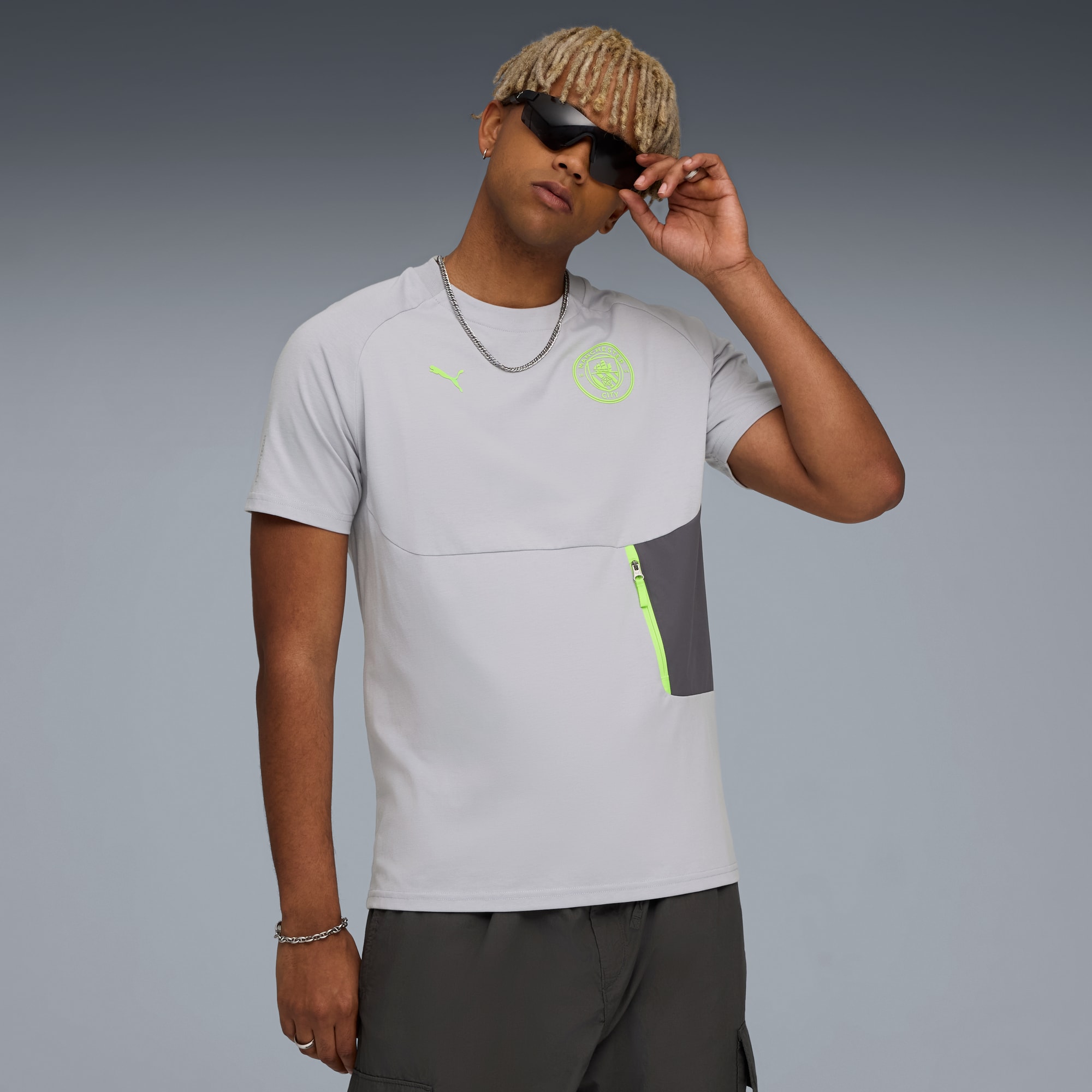 Un modèle pose devant un fond gris, portant un t-shirt gris et un pantalon foncé.