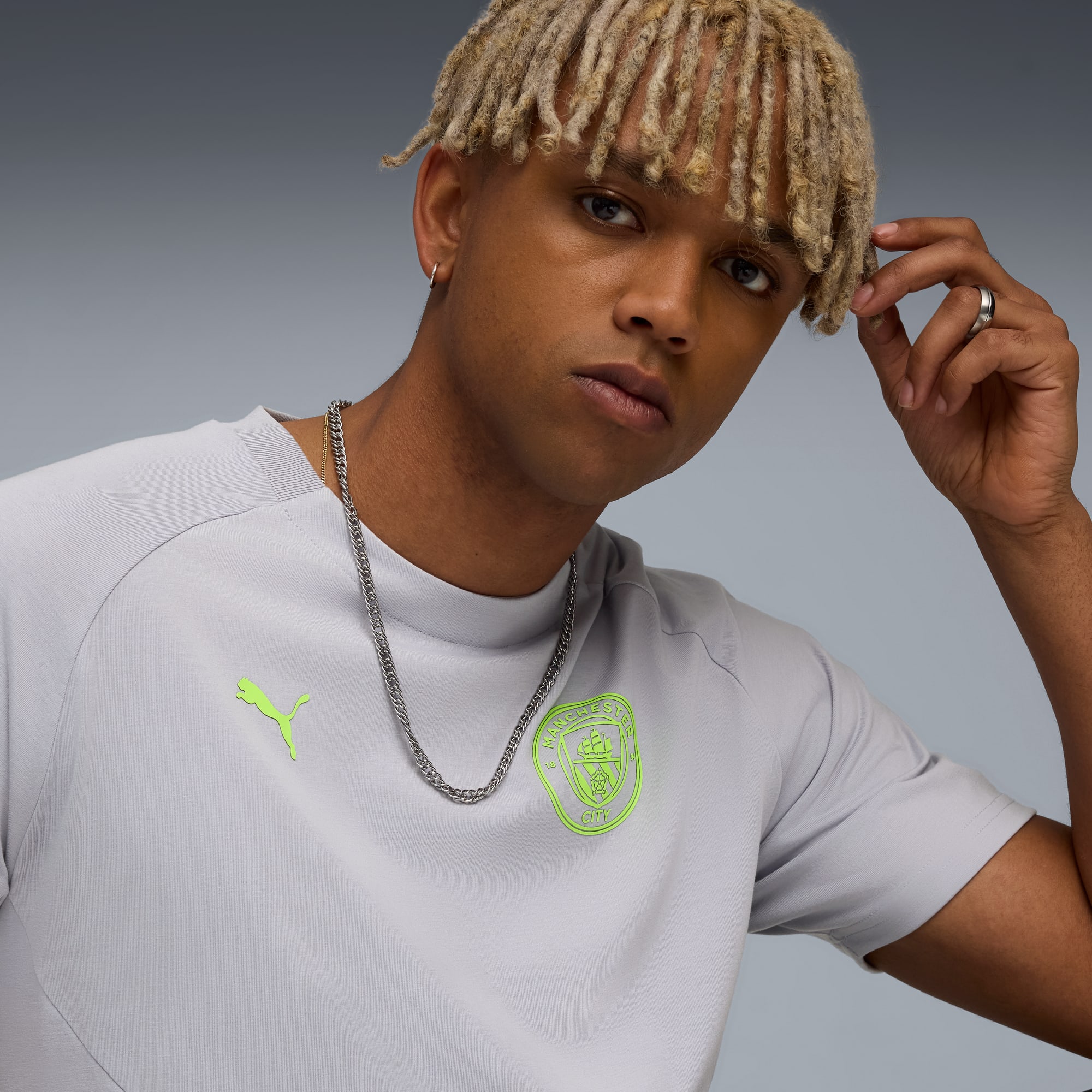 Un modèle pose sur fond gris, portant un t-shirt gris avec des logos vert citron.