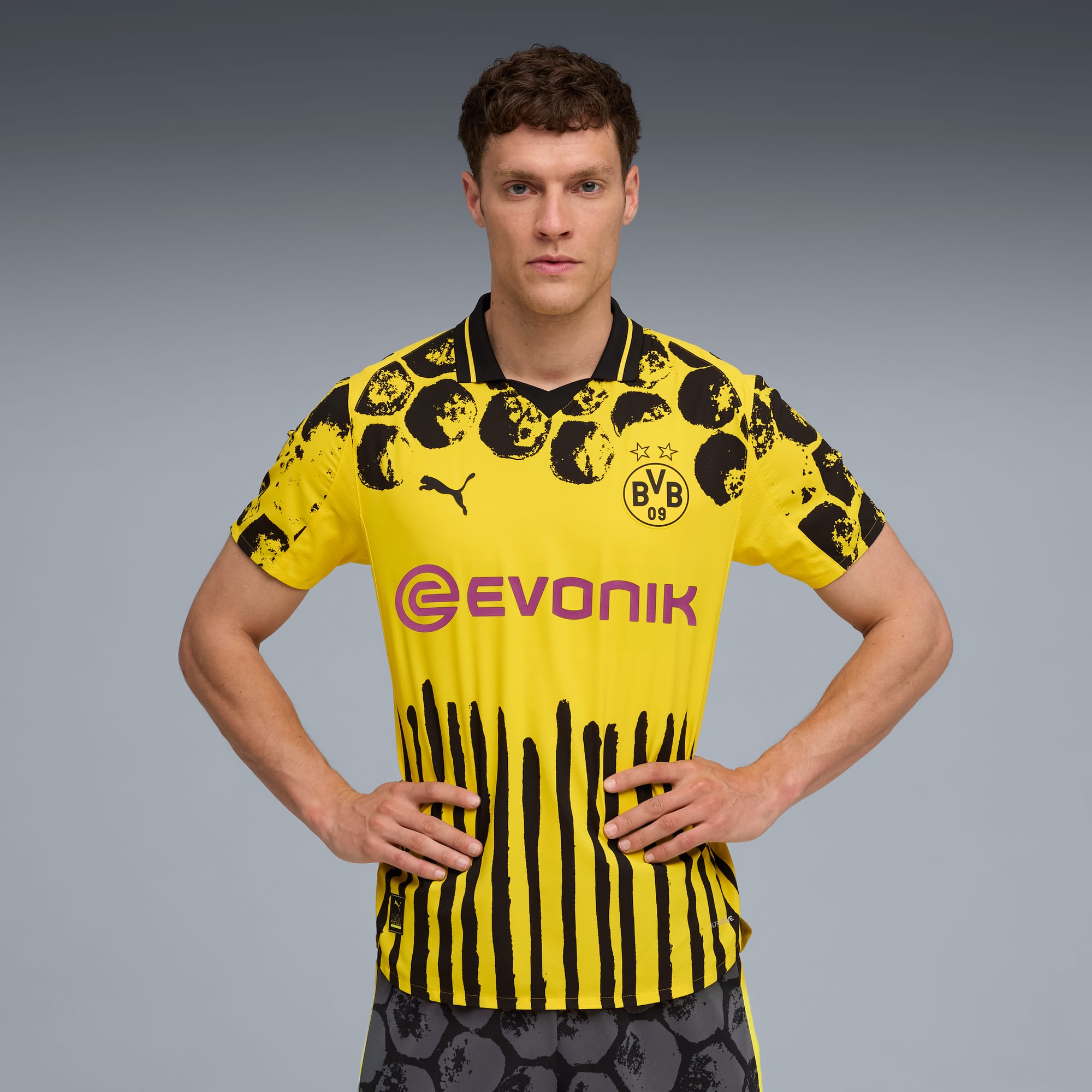 Un modèle pose sur fond gris avec un maillot de foot jaune et noir du Borussia Dortmund.