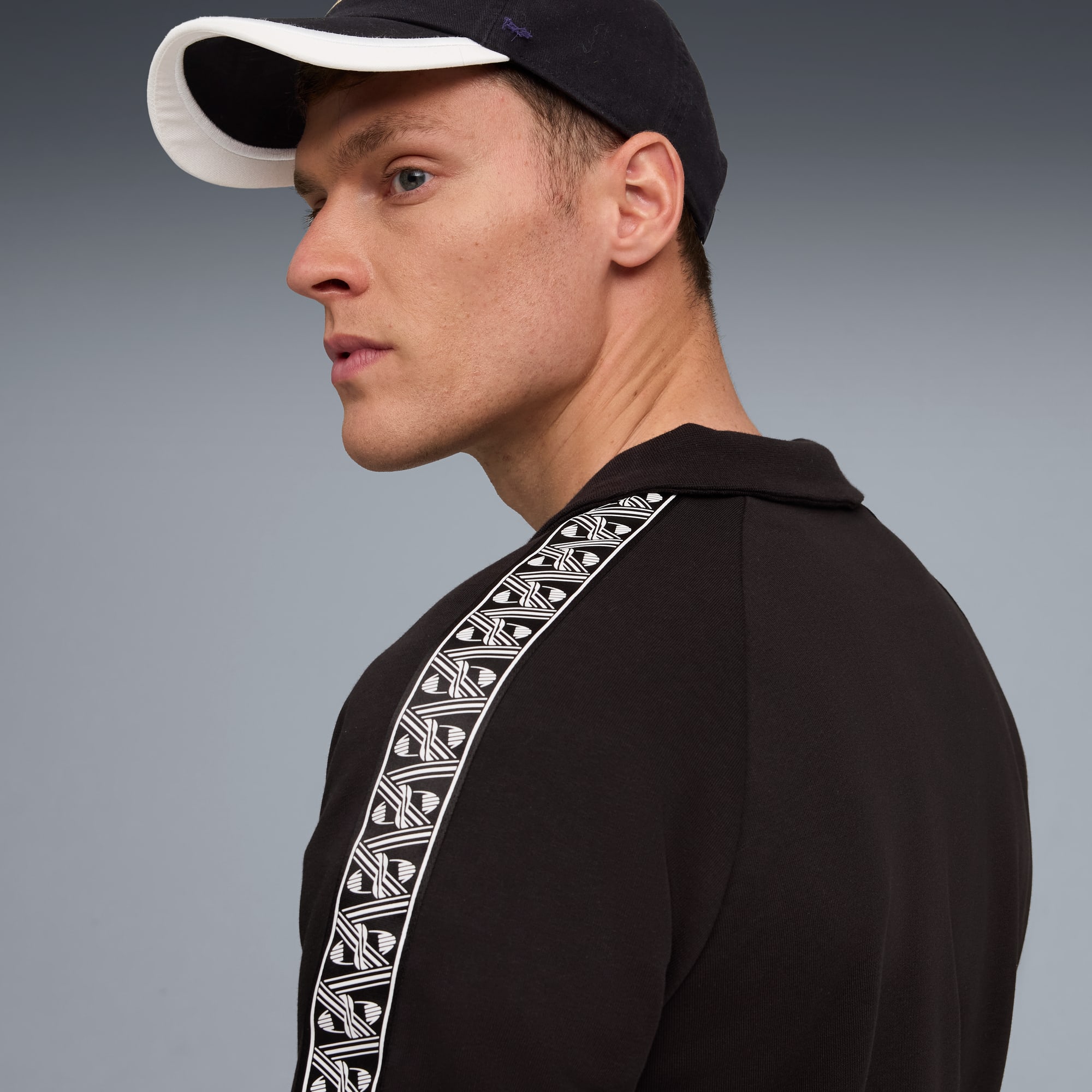 Sur fond gris, un modèle regarde à gauche, portant un haut noir à rayures et une casquette.