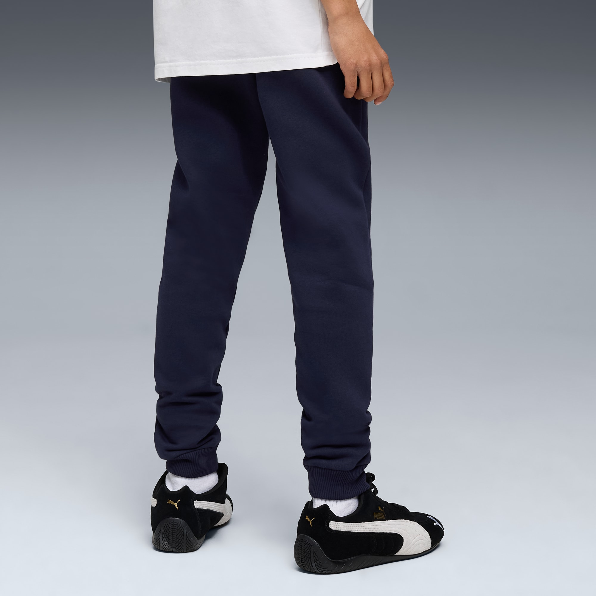 A model in front of a grey background wearing dark blue trousers and black and white trainers.