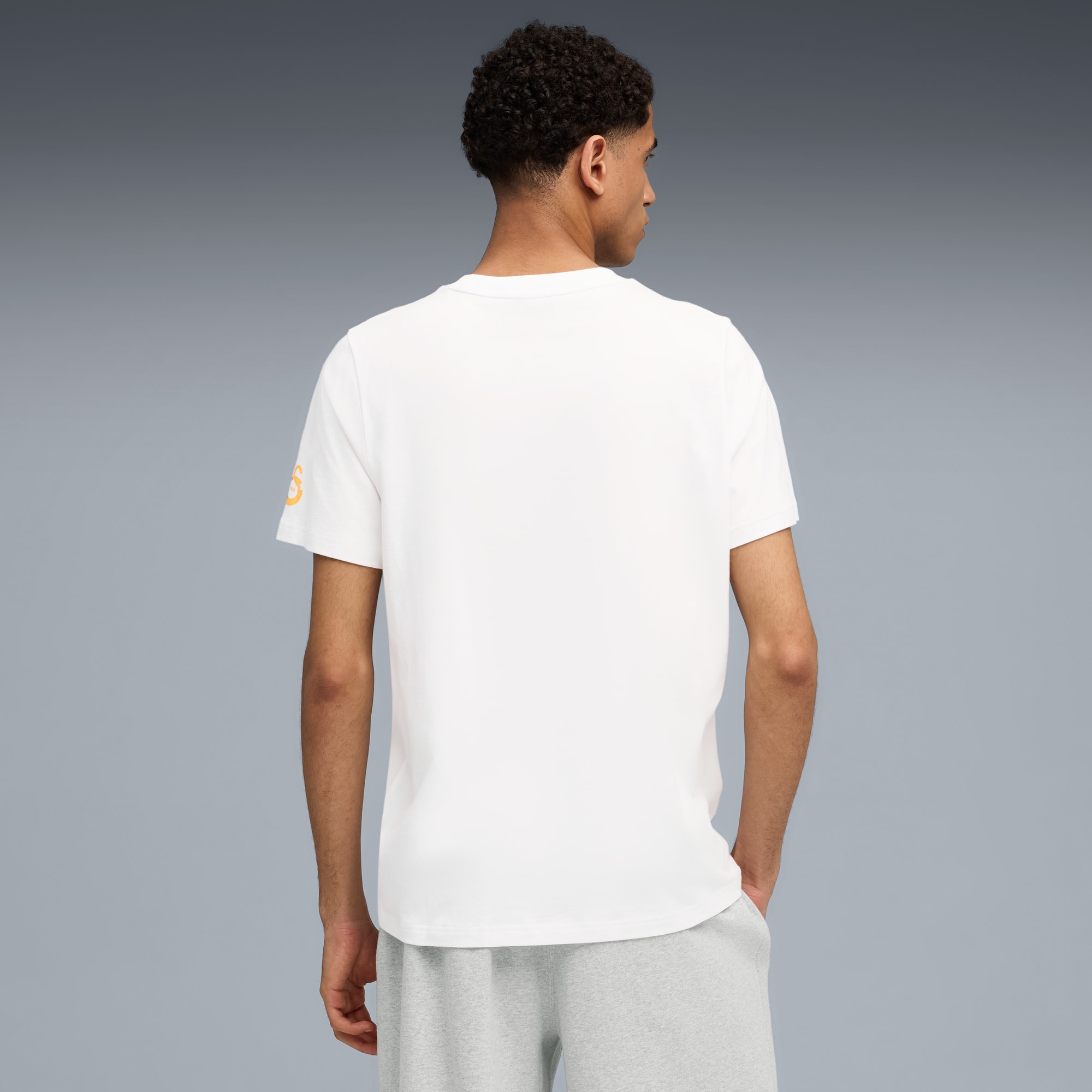 Een model staat tegen een grijze achtergrond, gekleed in een wit t-shirt en een grijze short.