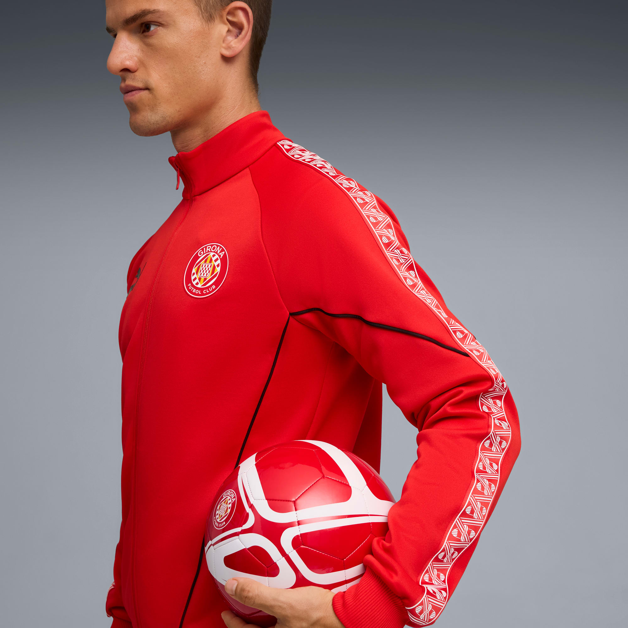 Su sfondo grigio, un modello tiene un pallone e indossa una giacca rossa con dettagli bianchi.