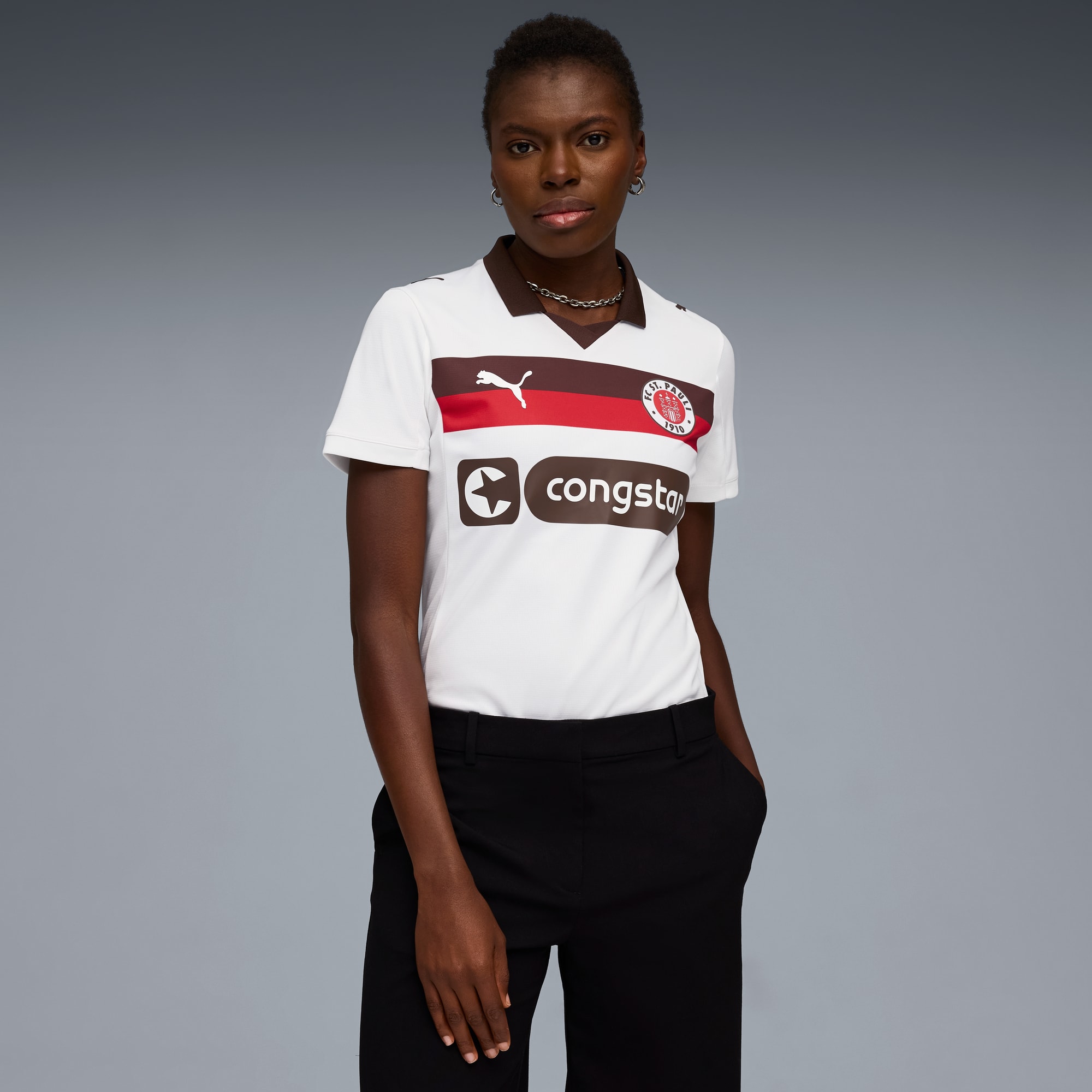 Ein Model posiert vor grauem Hintergrund, mit weißem T-Shirt und schwarzer Hose.
