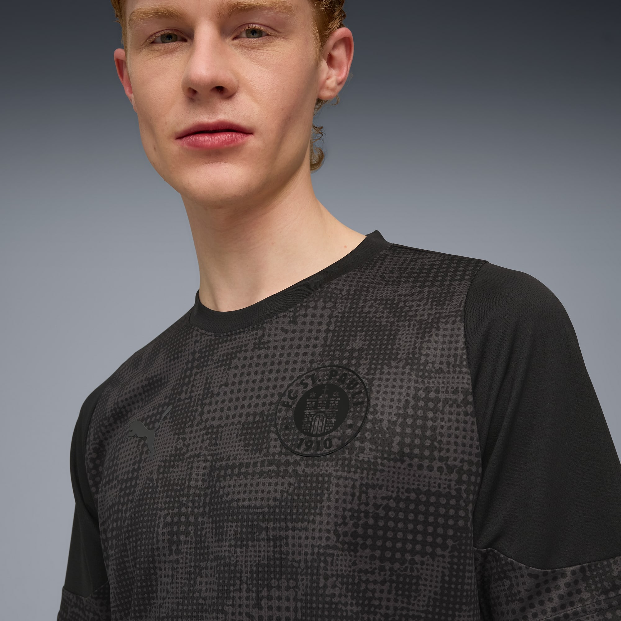 A model wears a black patterned t-shirt with a club logo against a grey backdrop.