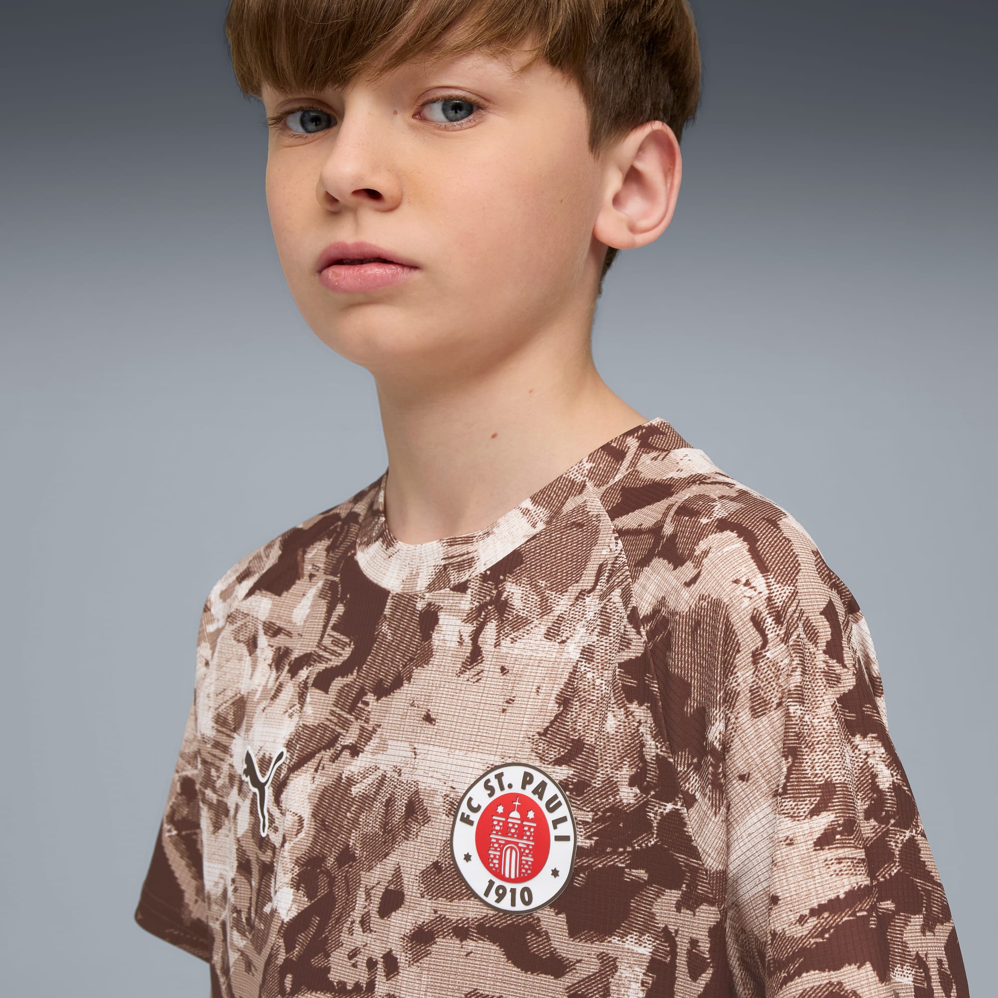 Model na szarym tle w brązowej koszulce FC St. Pauli we wzory.