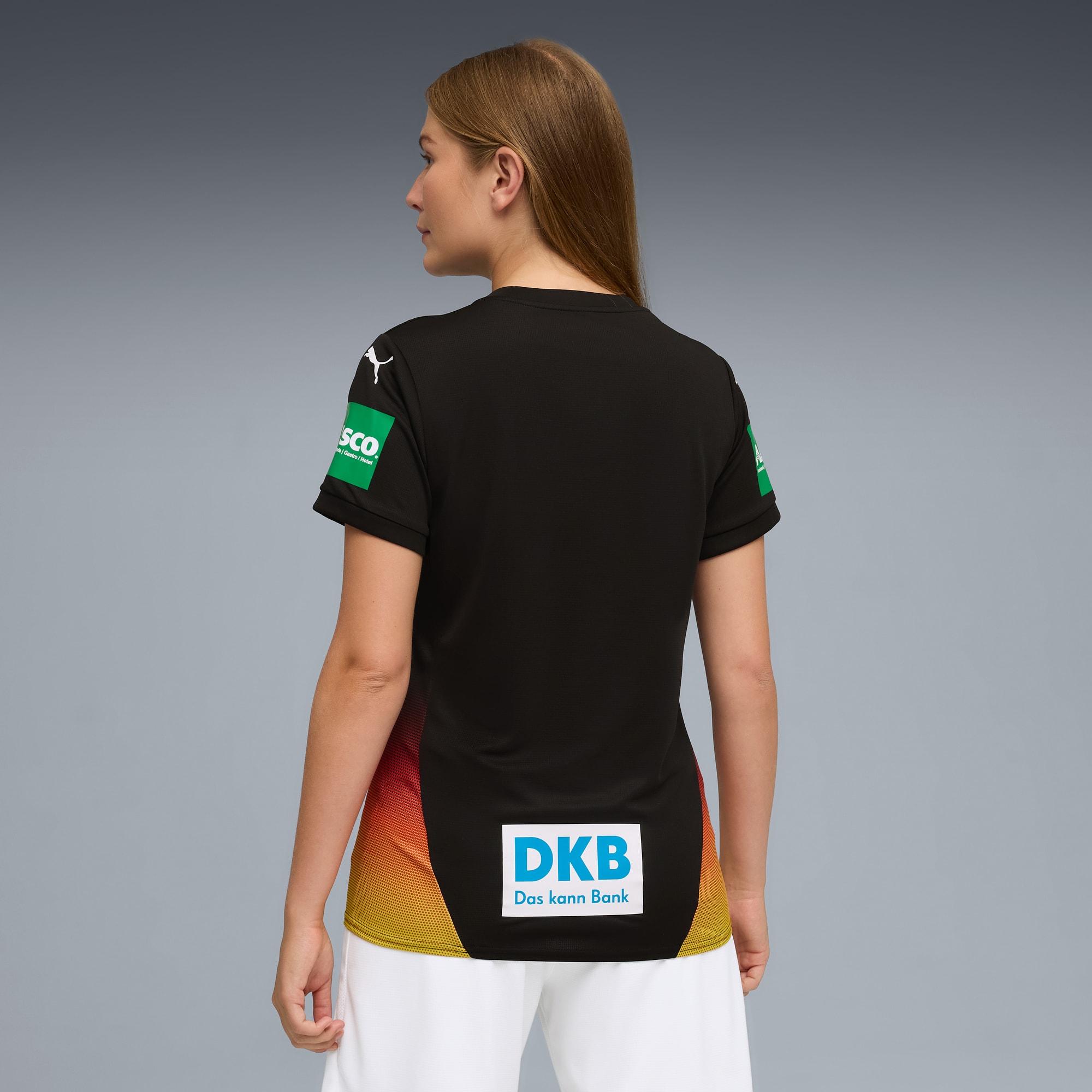 Una modella di spalle indossa una maglia nera con loghi su sfondo grigio.