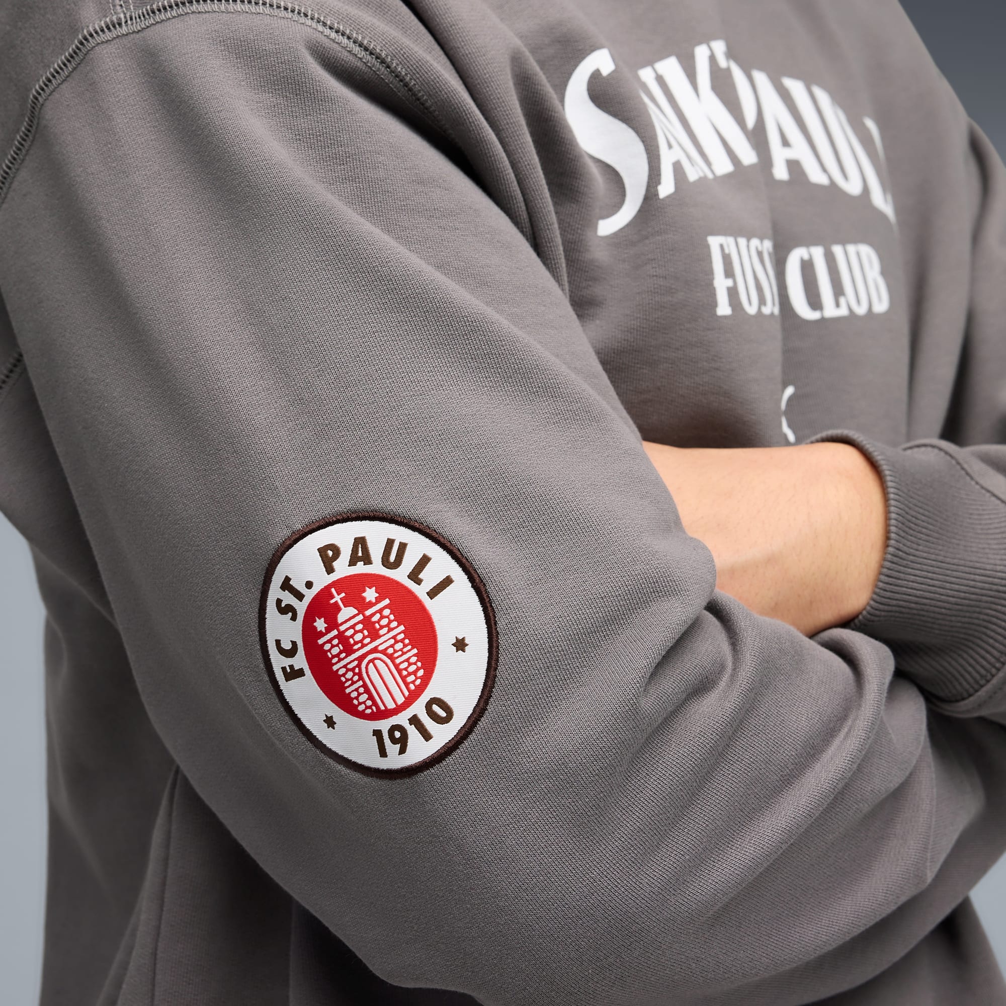A grey sweatshirt with a FC St. Pauli badge on the sleeve, arms crossed.