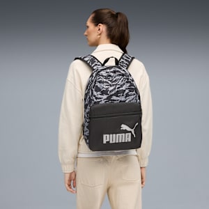Against grey, a model wears a patterned backpack, facing left, with ponytail.