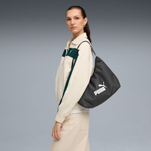 Against grey, a model poses with a dark shoulder bag and cream-coloured jacket.