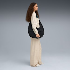 A model carries a large black bag over her shoulder against a grey backdrop.