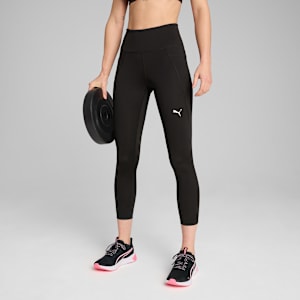 Against a grey backdrop, a model holds a weight plate wearing black leggings and trainers.