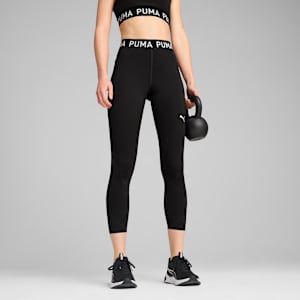 On grey, a model holds a kettlebell, wearing black leggings, sports bra and trainers.
