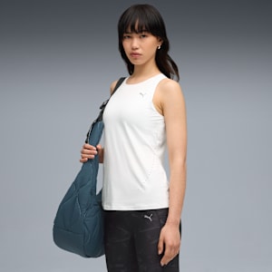 Against grey, a model wears a white top and patterned bottoms, carrying a blue bag.